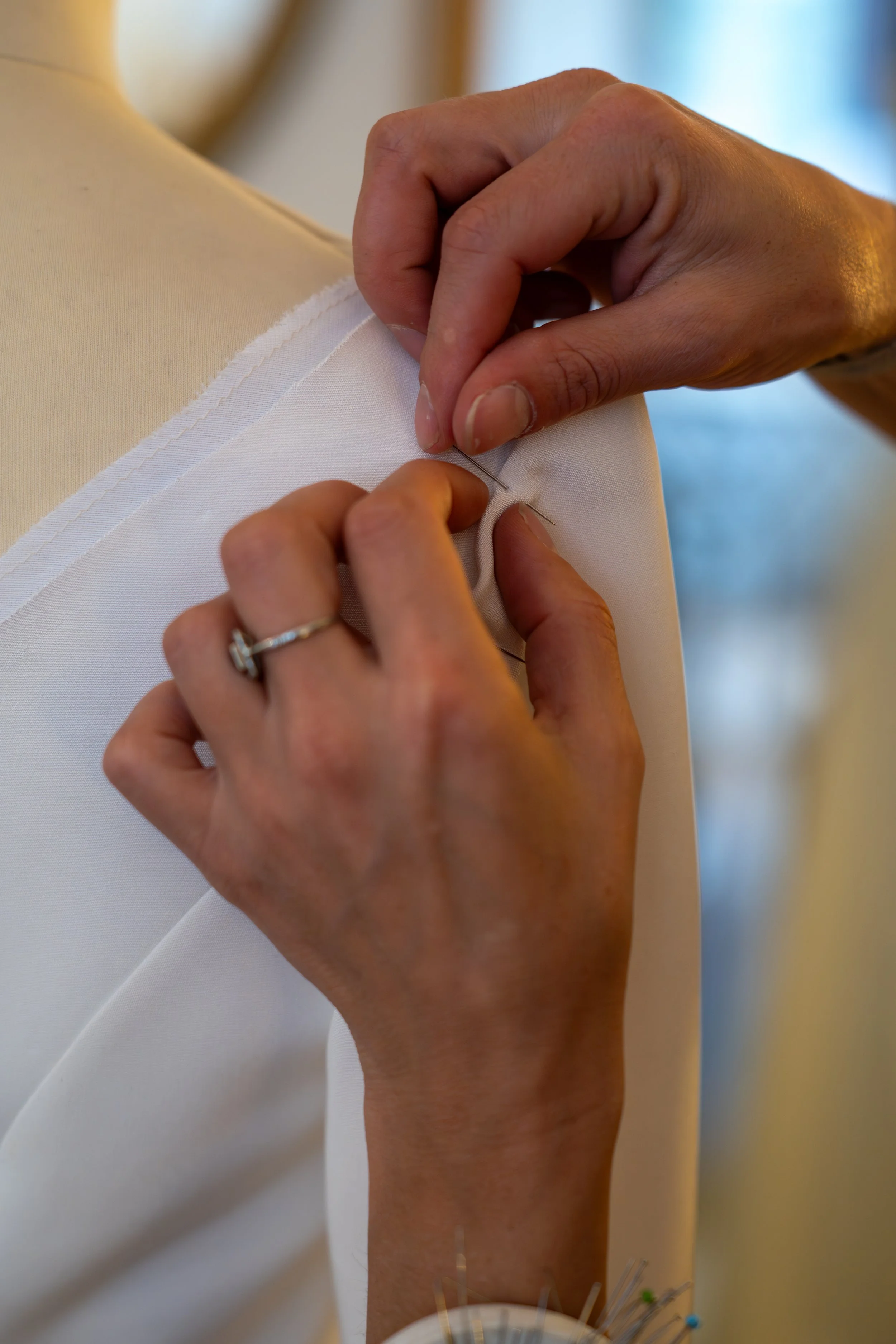 Des mains cousant une robe blanche sur un mannequin.