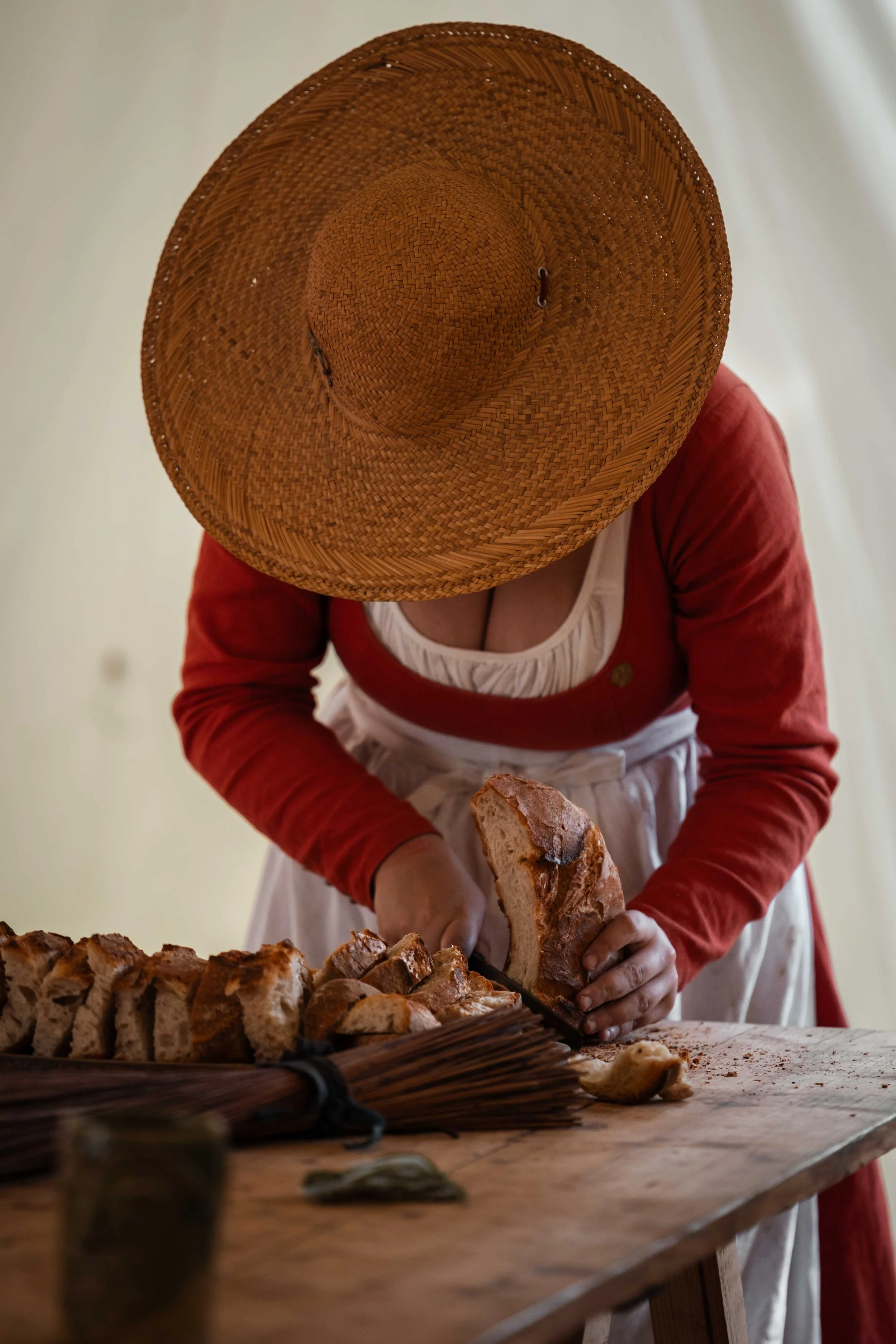 Personne portant un chapeau en panama coupe un pain dans une cuisine rustique.