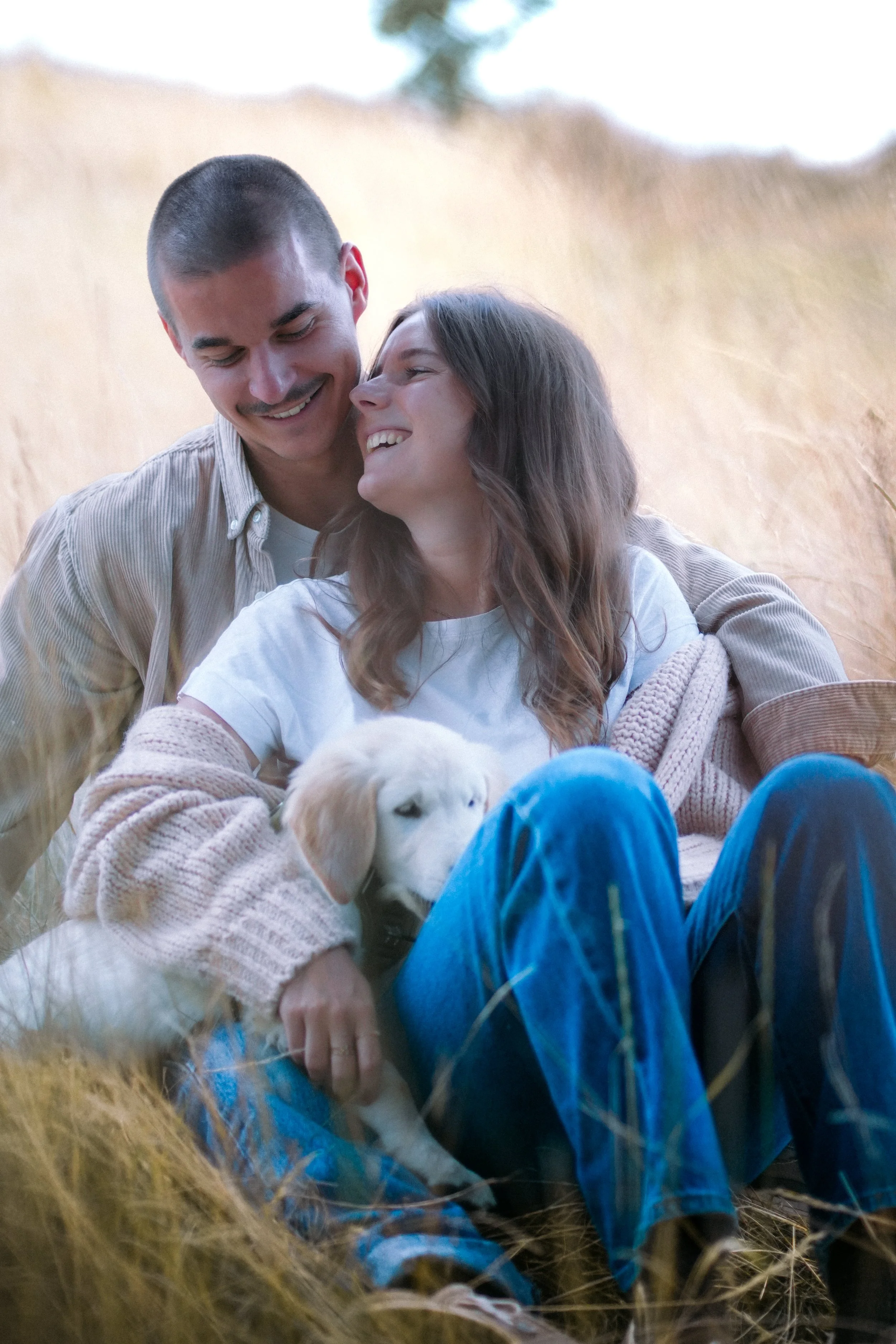 Un couple souriant avec un chiot blanc dans un champ d'herbes sèches, heureux et proches.