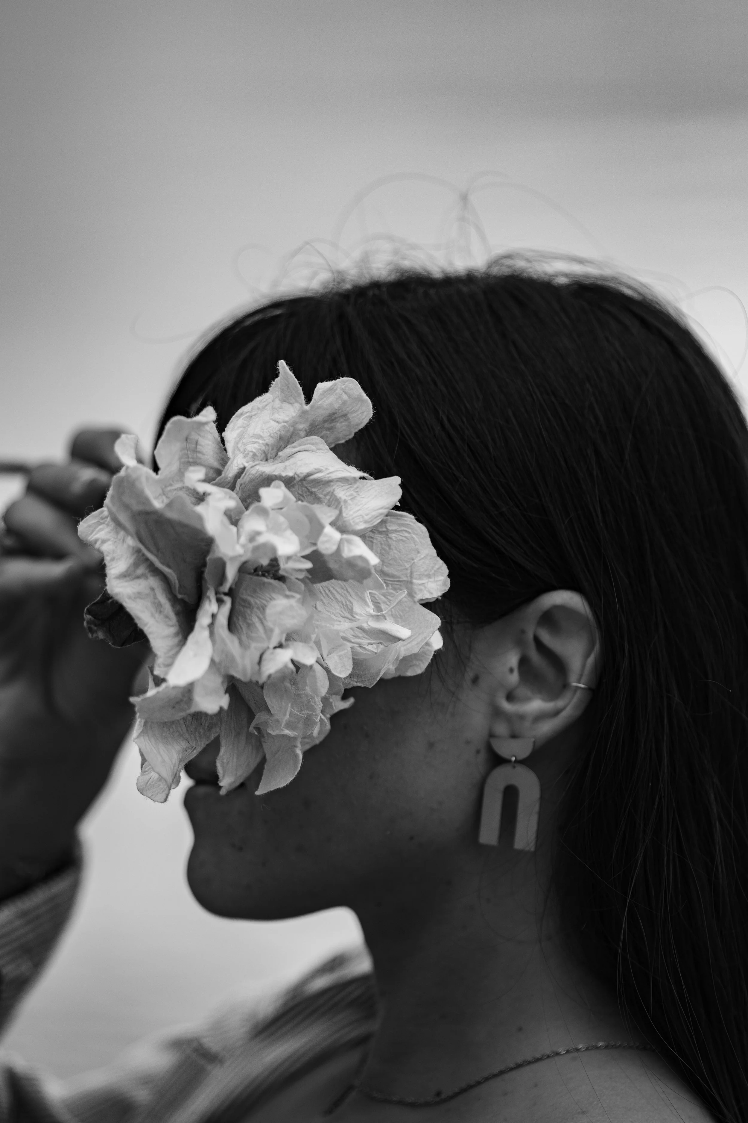 Une femme porte une grande fleur sur le côté de la tête et a des boucles d'oreilles en forme d'arche, en noir et blanc.