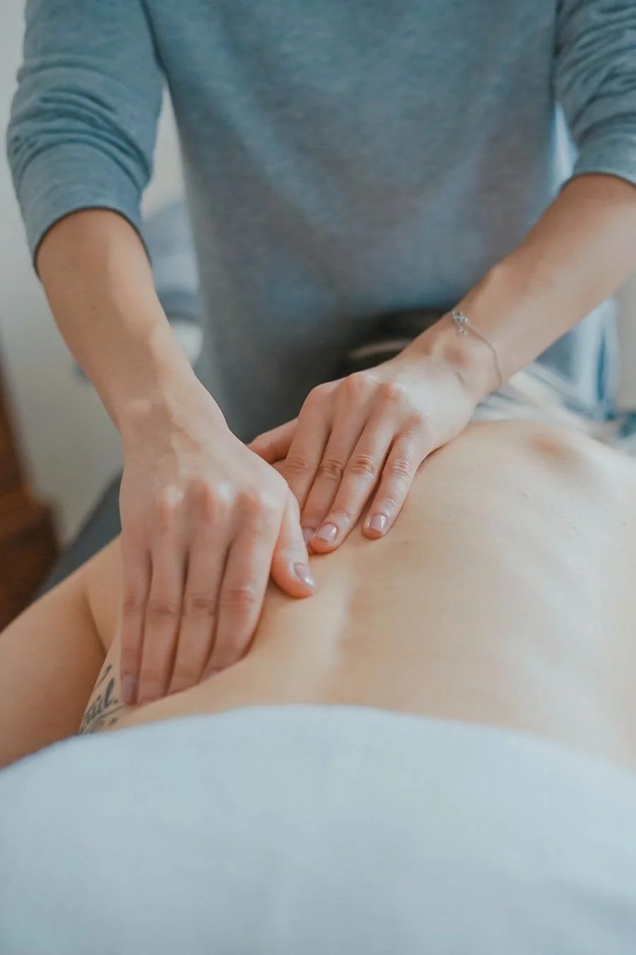 Une personne reçoit un massage ou une thérapie manuelle sur le dos d'une autre personne, avec un praticien utilisant ses mains pour appliquer une pression.