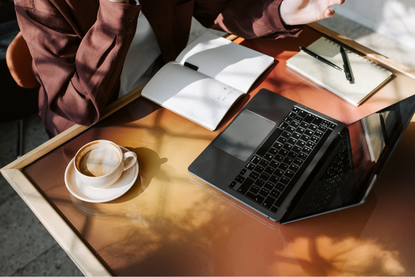 Laptop, notebook and flat white on copper table, business advisory working session