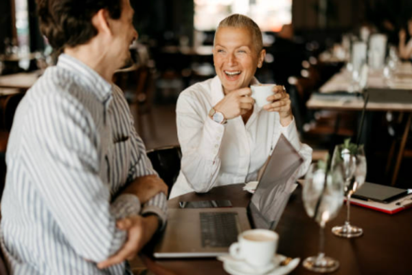 A male and female professional laughing over coffee and laptop, genuine client advisory meeting