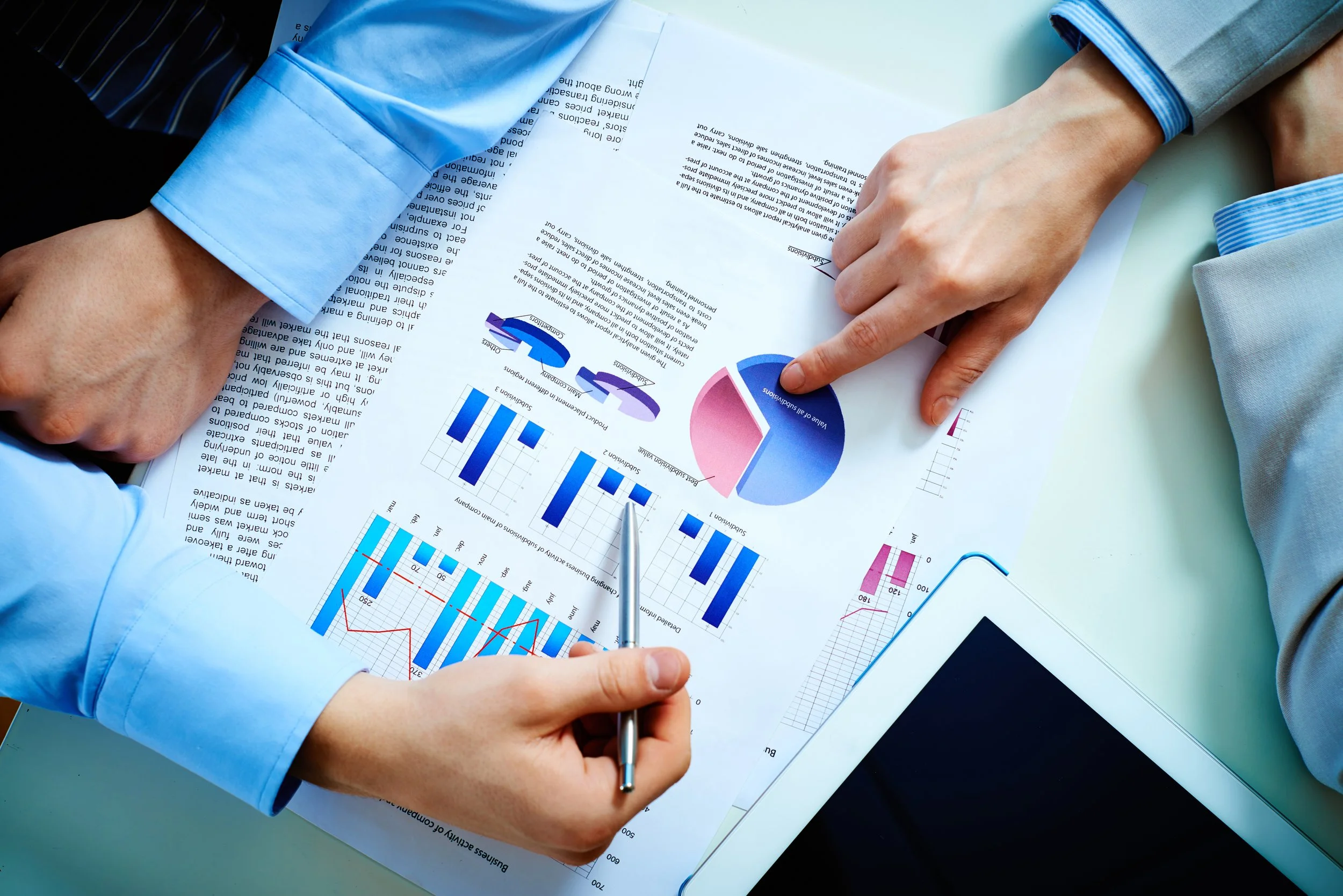 Two individuals analyzing business charts and graphs on printed documents, with a tablet on the table.