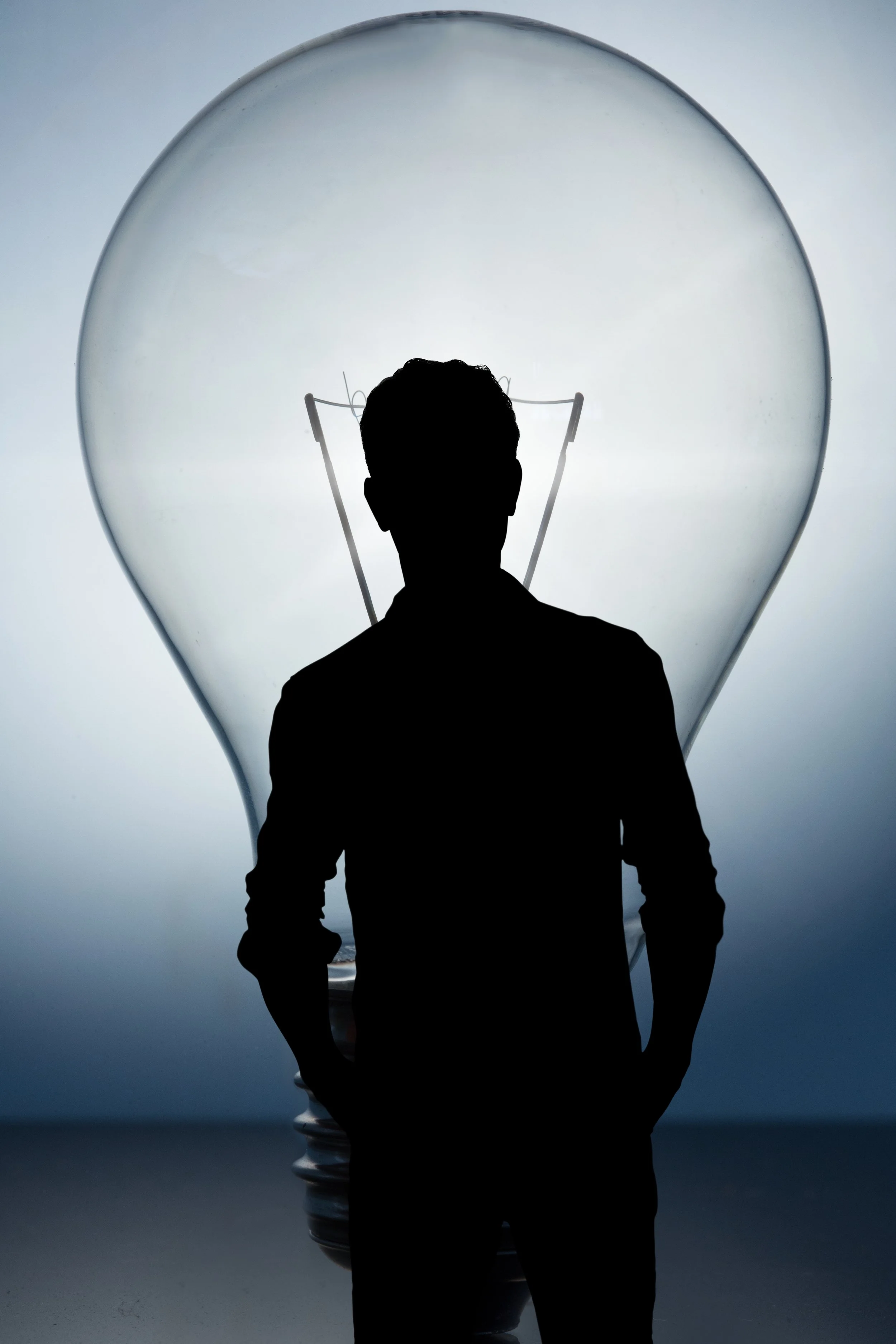 Silhouette of a person standing in front of a large lightbulb.