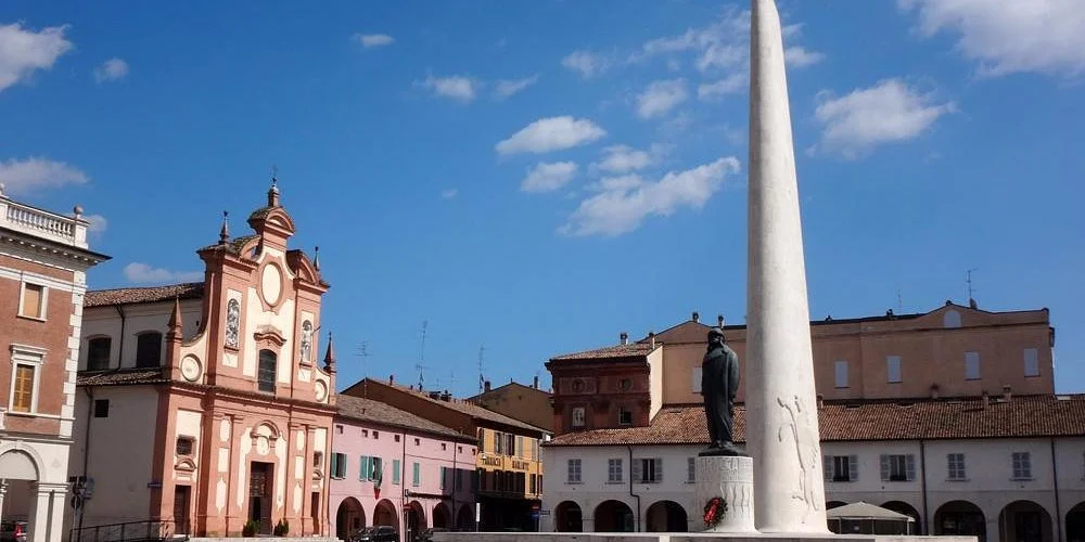 Una piazza con un obelisco, una statua di un uomo, e una chiesa rosa in stile barocco.
