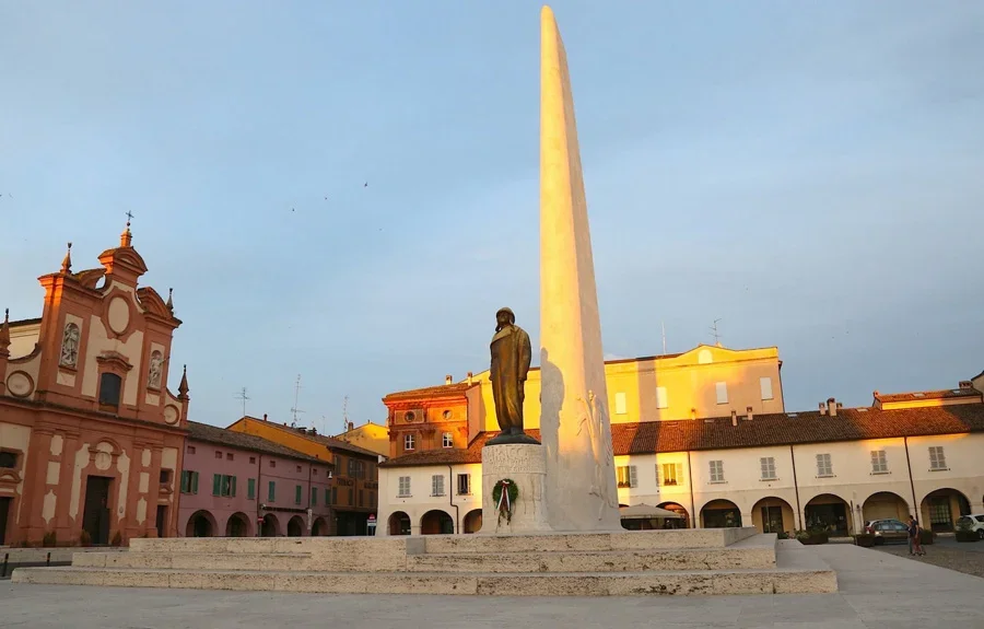 Piazza con monumento e statue, edifici storici, inizio tramonto.