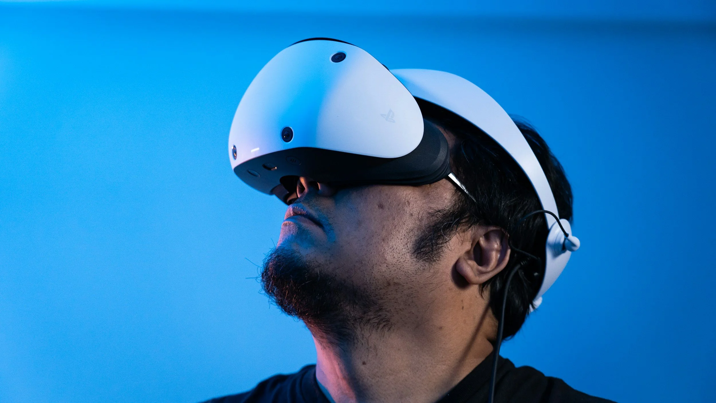A person wearing a white virtual reality headset with a black strap, facing left against a blue background.