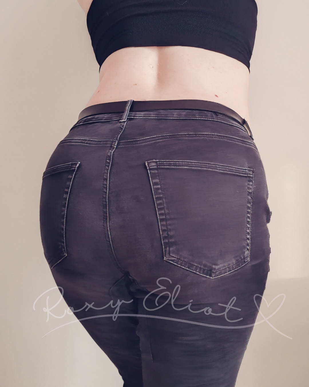 Back view of a person wearing black jeans and a black crop top, showing their lower back and buttocks.