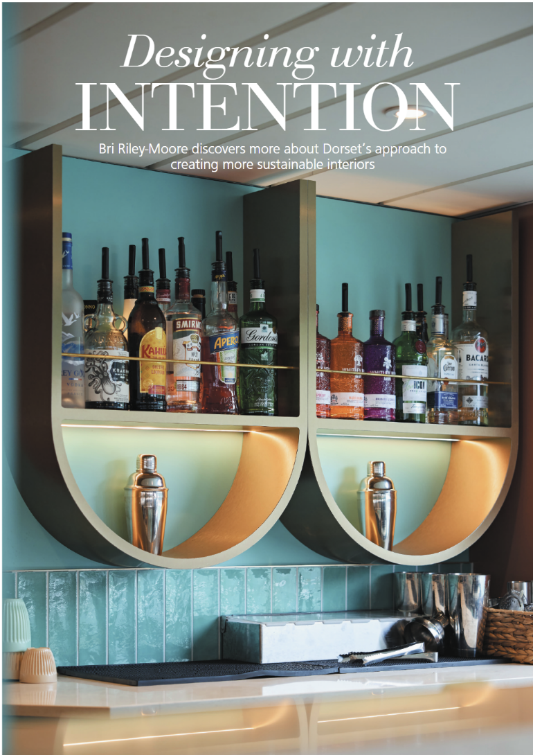 A bar shelf with assorted liquor bottles, illuminated behind a turquoise wall, with bar tools and accessories below.