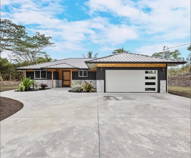 Modern single-story house with a concrete driveway, a two-car garage, and a landscaped front yard under a partly cloudy sky.