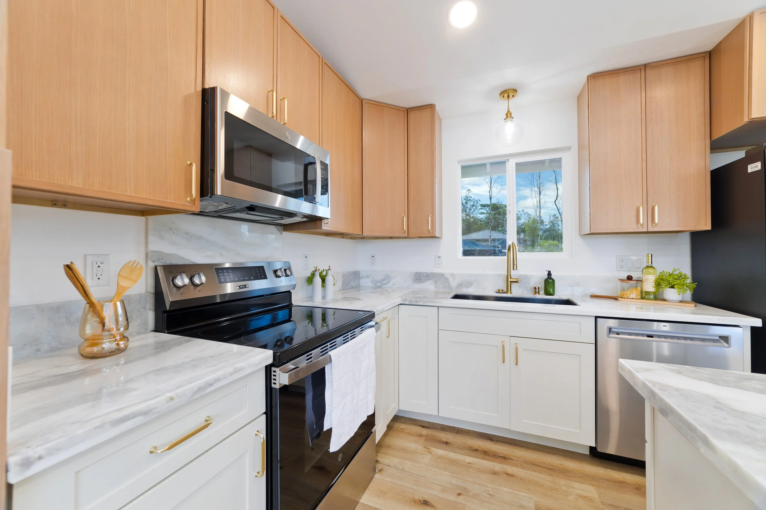 Modern kitchen with white and wood cabinets, stainless steel appliances, a window over the sink, and light wood flooring