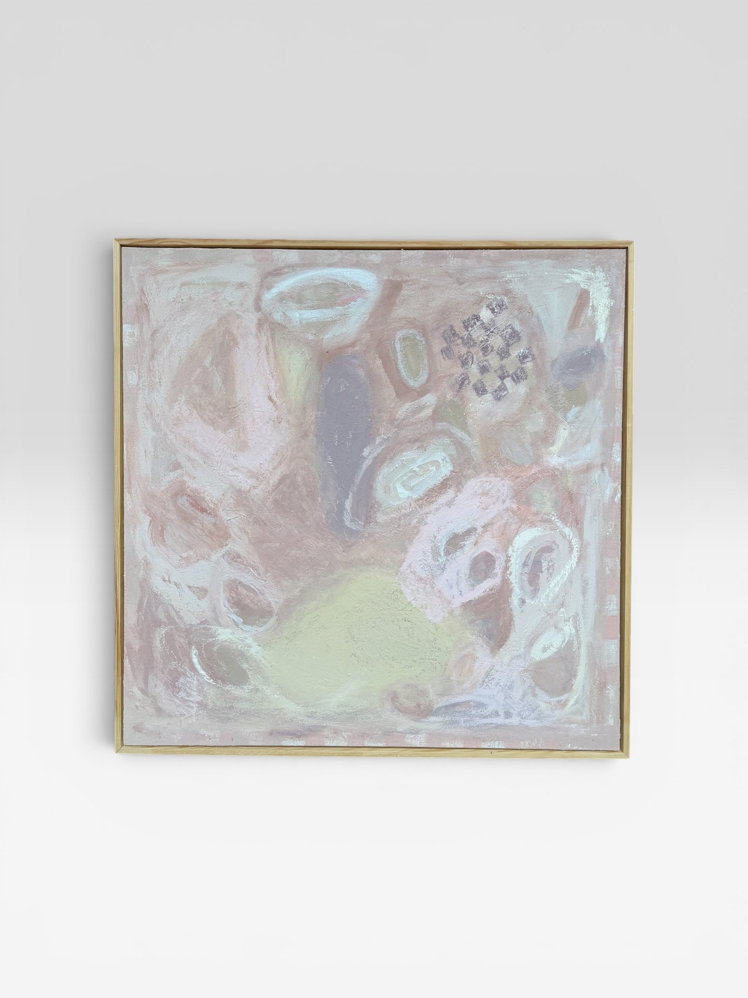 An abstract painting with soft pastel colors and swirling shapes, framed in a light wooden frame, hanging on a plain white wall.