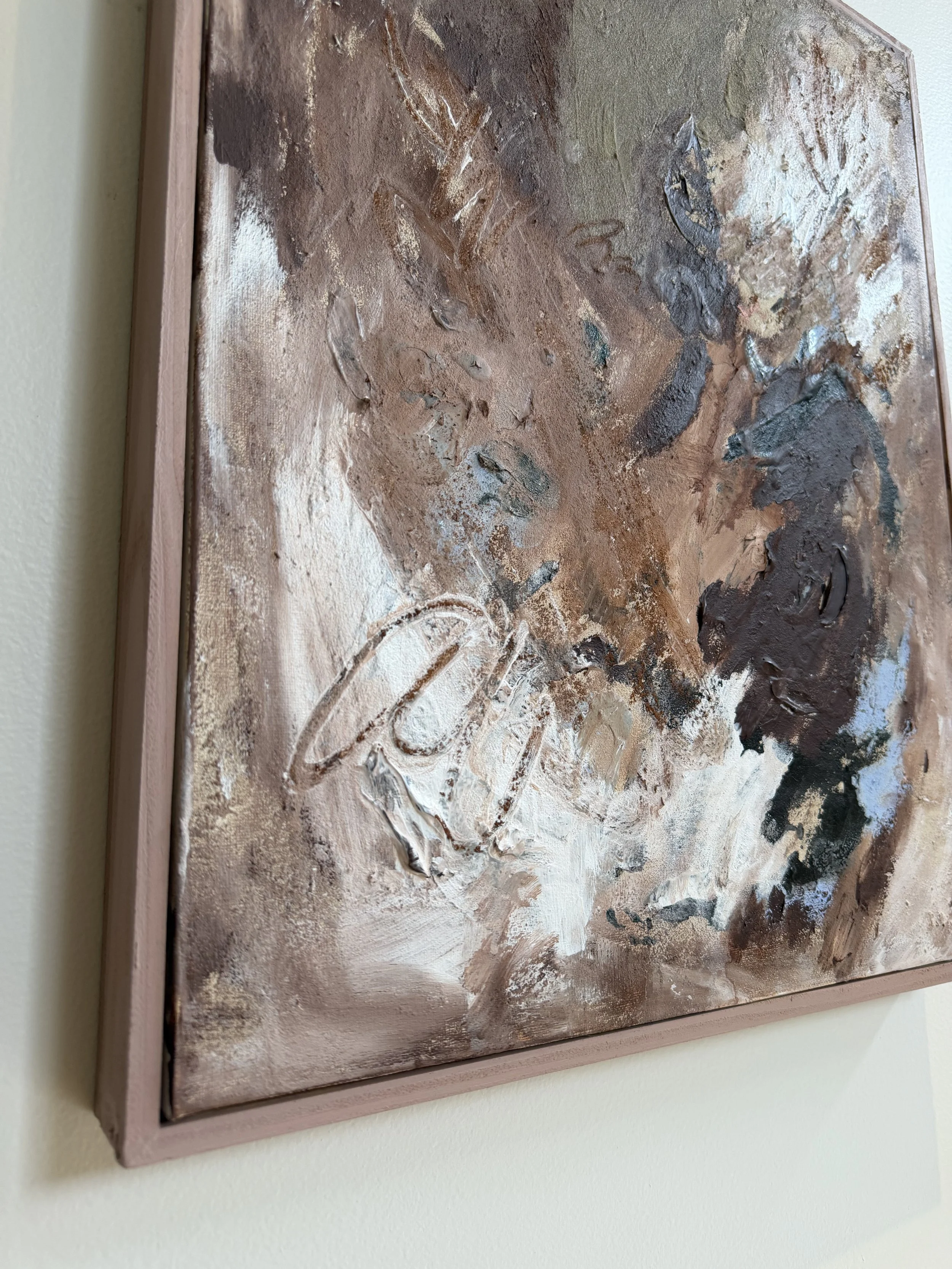 Abstract textured painting with earthy tones and a wooden frame hanging on a cream-colored wall.