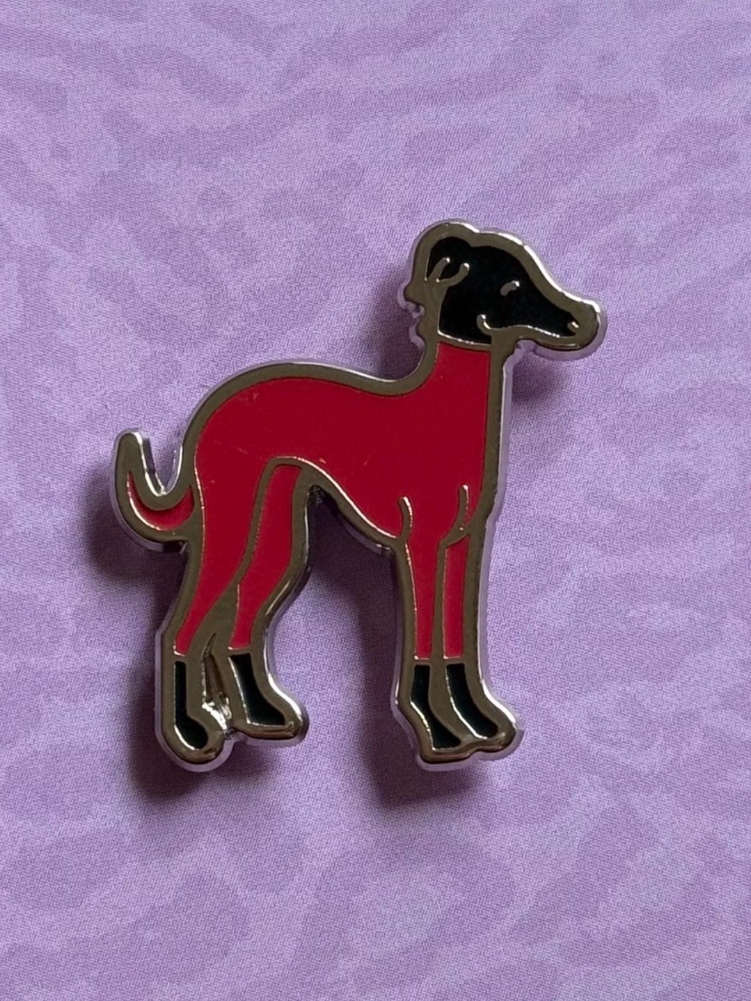 A pin featuring a stylized dog with a red body, black head and legs, set against a purple background.