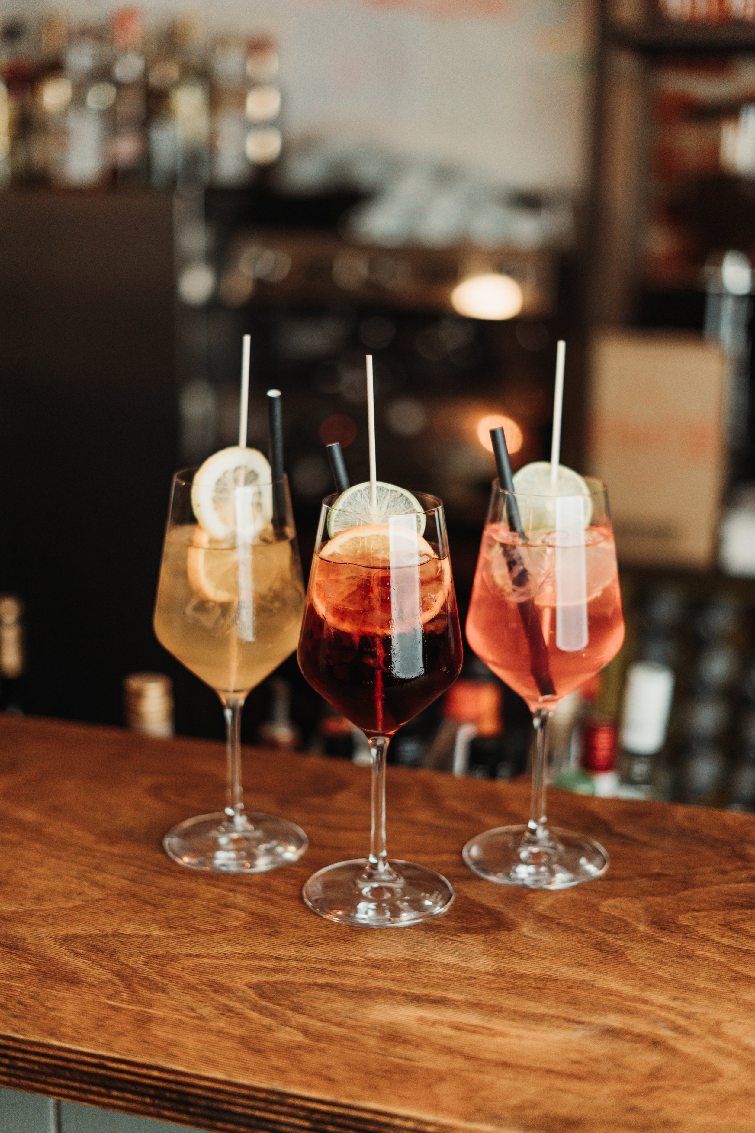 Drei bunte Cocktails mit Zitronenscheiben und Strohhalmen auf Holztisch in Bar