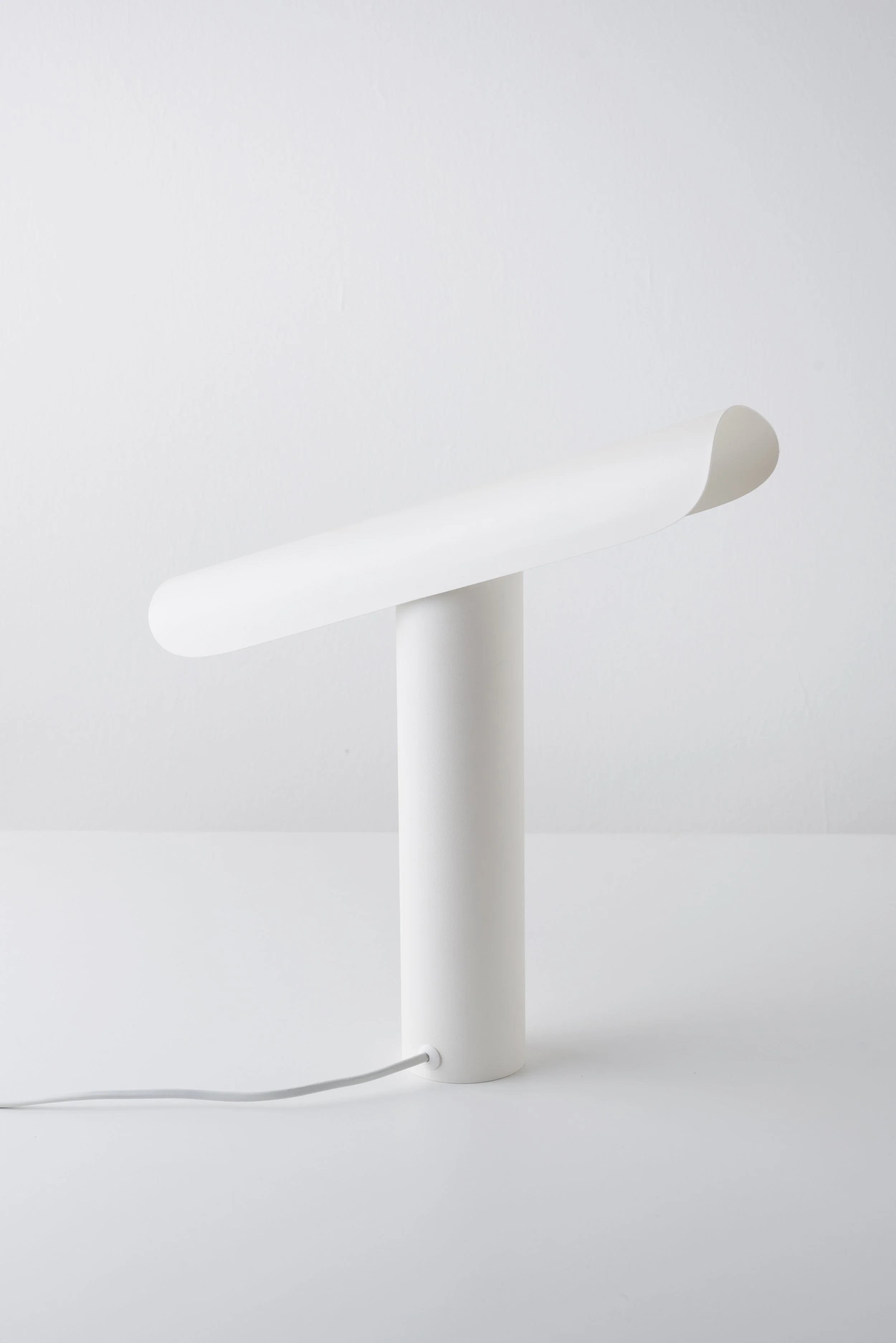 T Lamp illuminating a workspace, with a sculptural geometric form and tiltable head for versatile lighting angles.