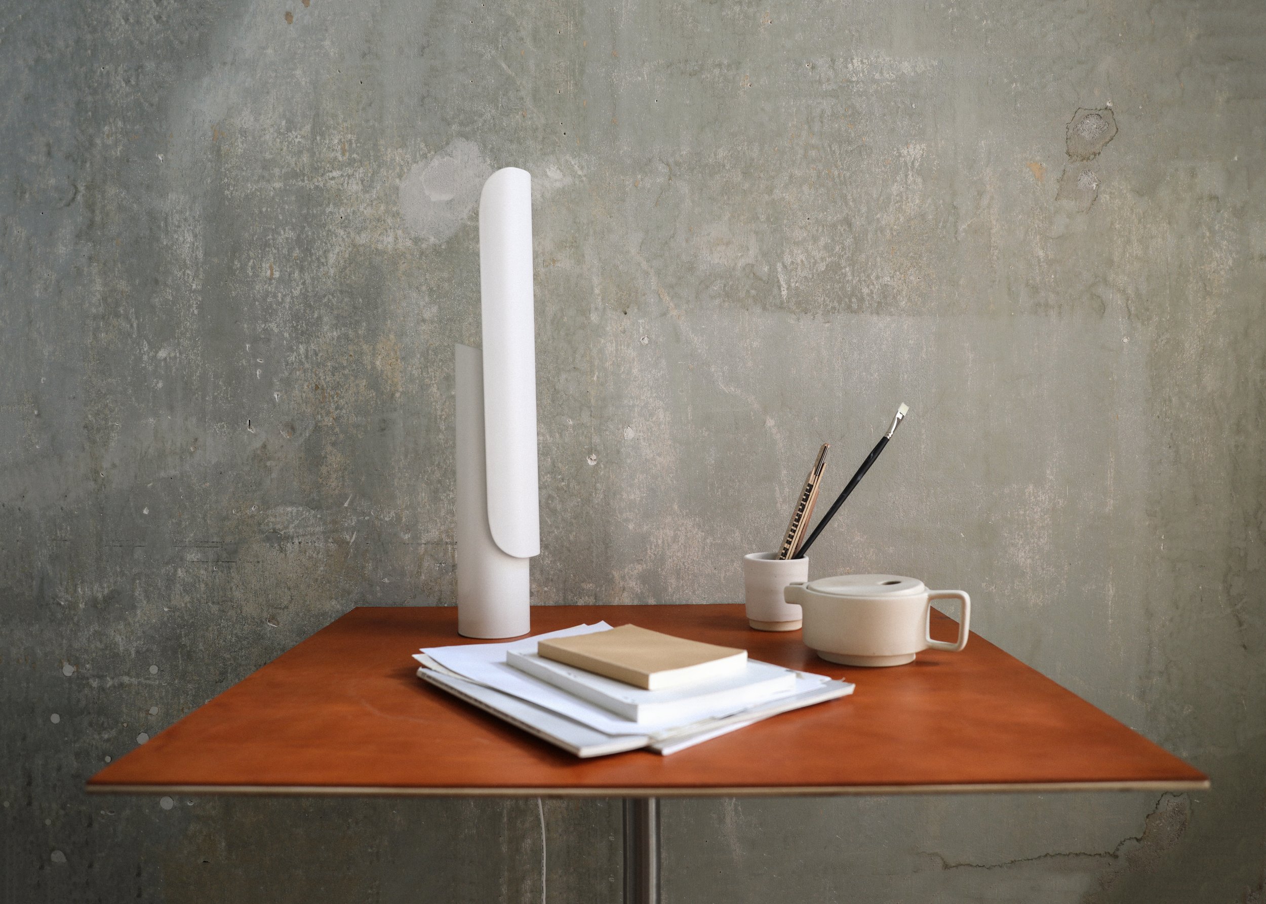 T Lamp illuminating a workspace, with a sculptural geometric form and tiltable head for versatile lighting angles.