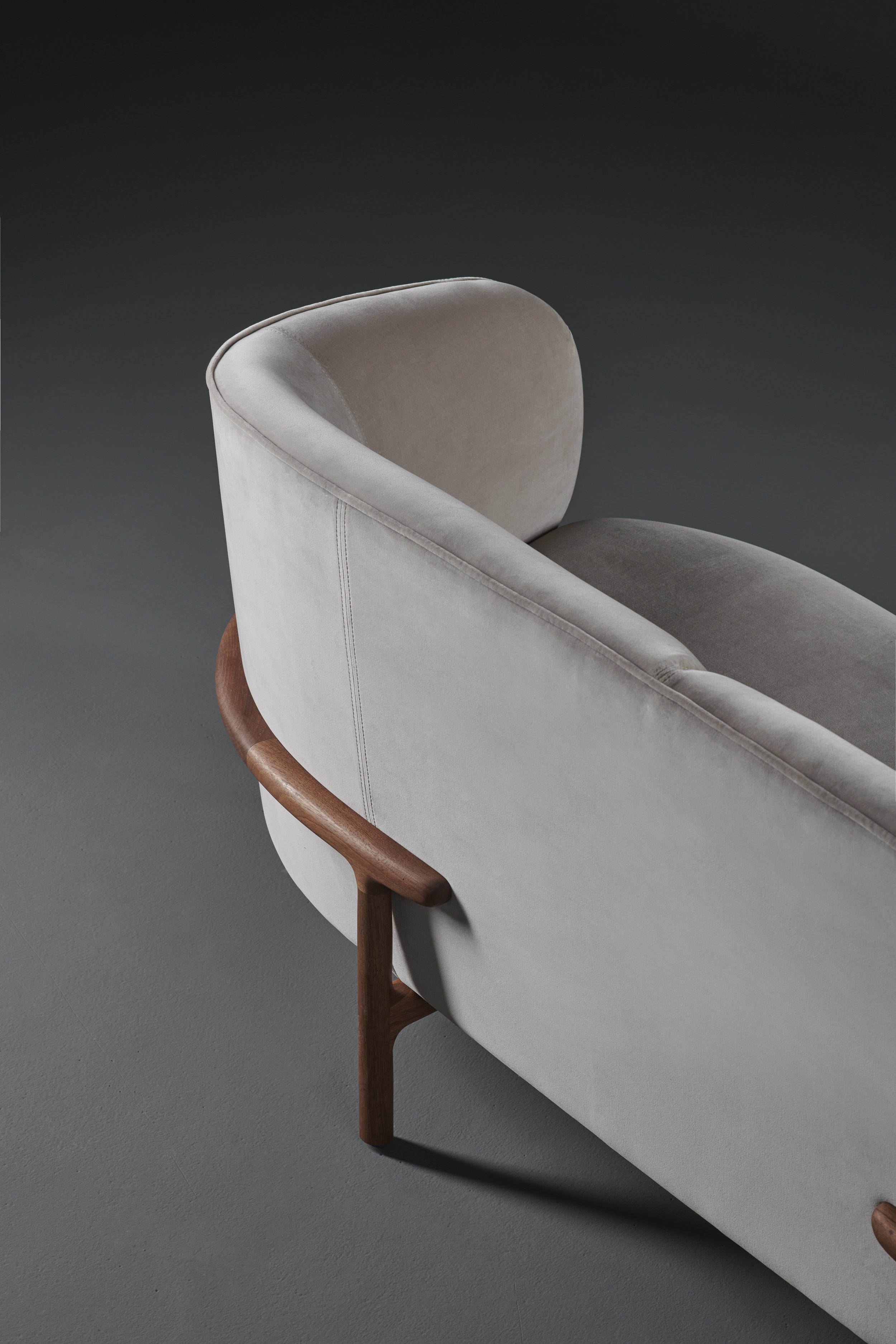 Three-quarter view of the Mela Lounge Two-Seater showing its smooth, rounded upholstery and finely crafted wooden base.