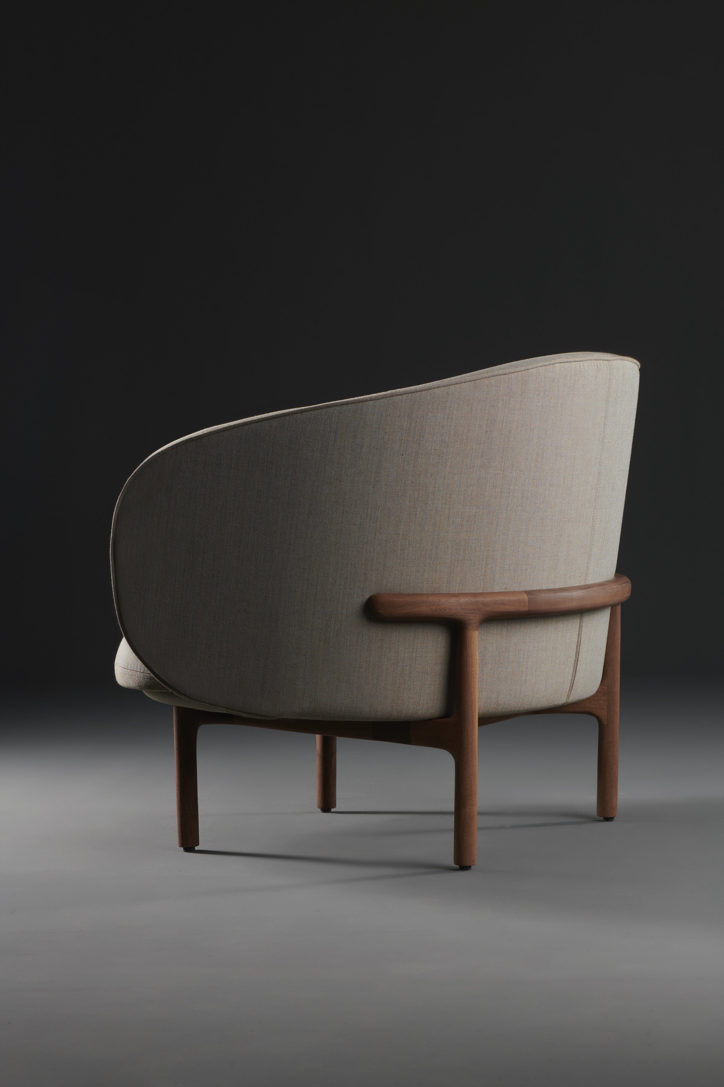 Three-quarter view of the Mela Lounge Trimmed showing softly contoured upholstery and a precisely crafted wooden base.
