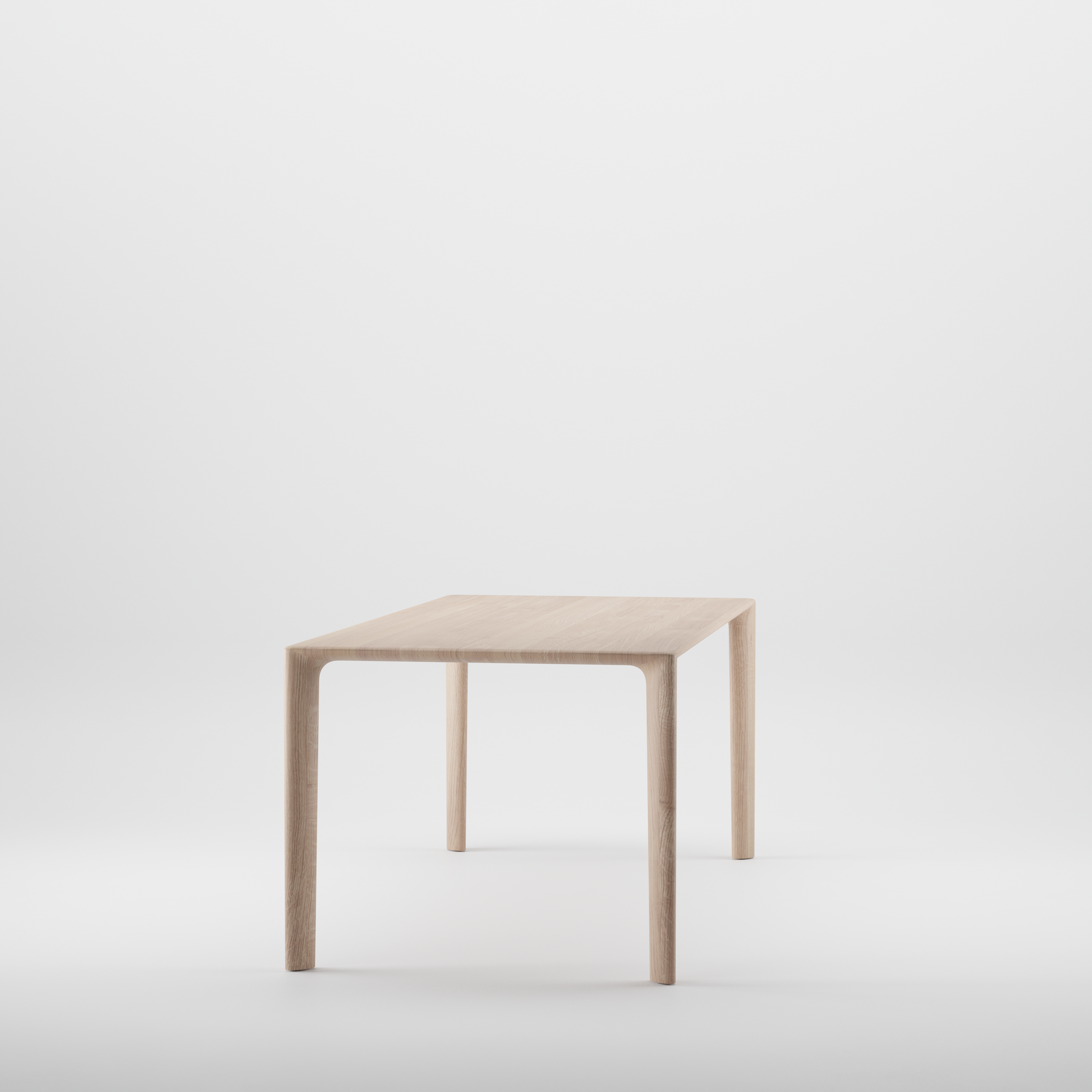 Three-quarter view of the Mela Table showing its smooth, sculpted wooden top and rounded corners.