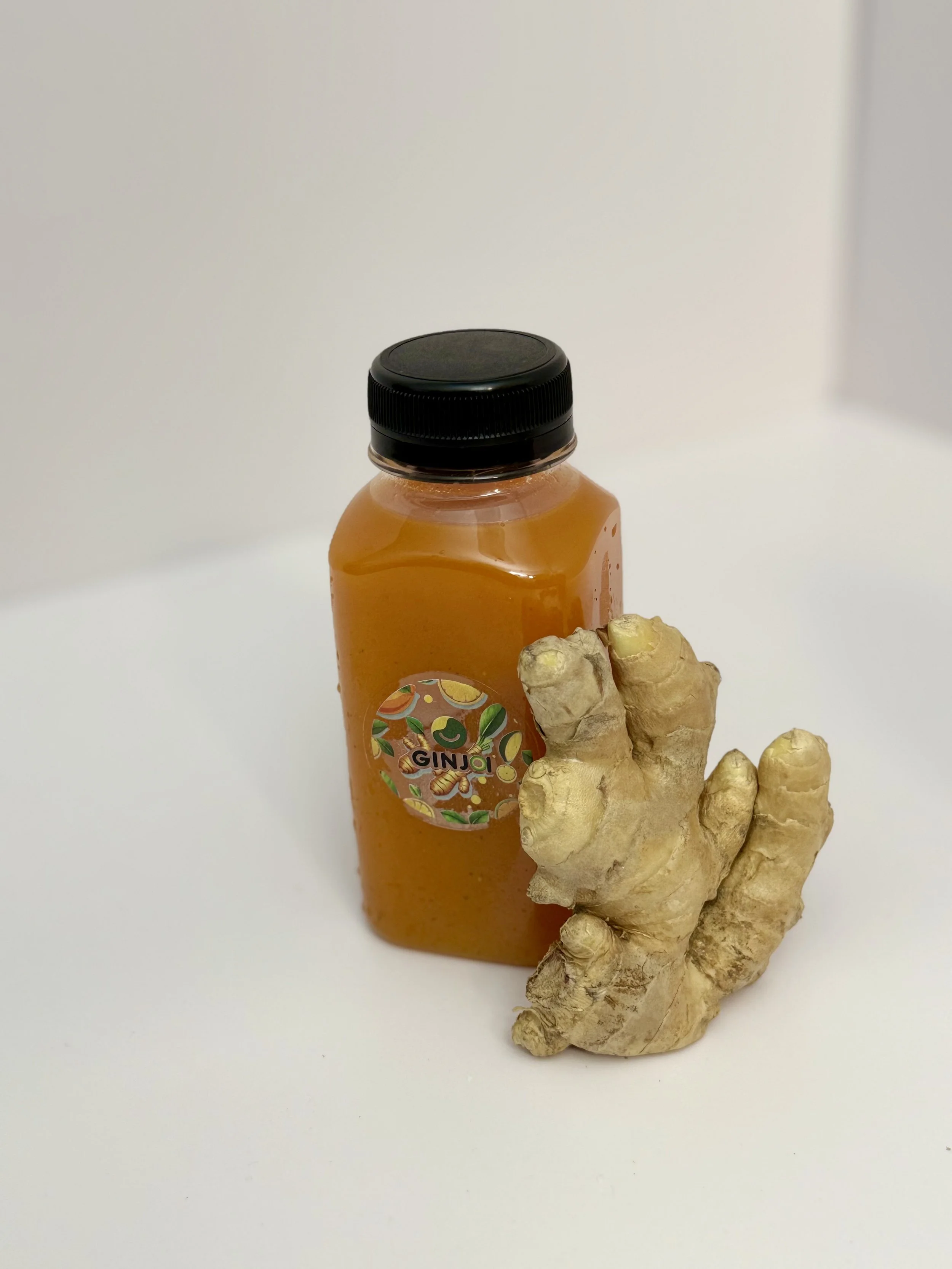 A bottle of ginger juice labeled 'Ginji' and a piece of fresh ginger root on a white surface.