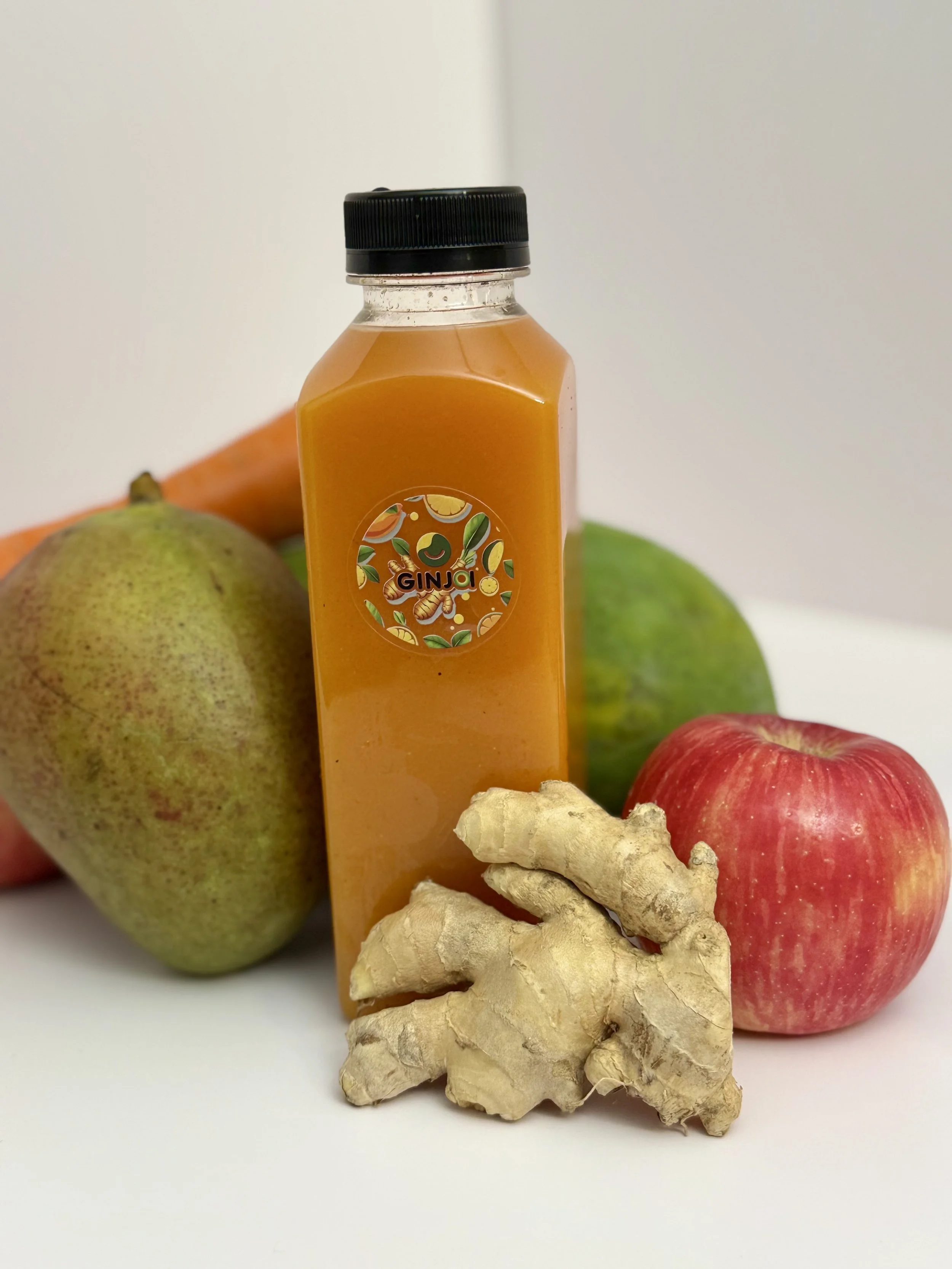 A bottle of orange juice surrounded by an apple, pear, cucumber, carrot, and ginger on a white background.