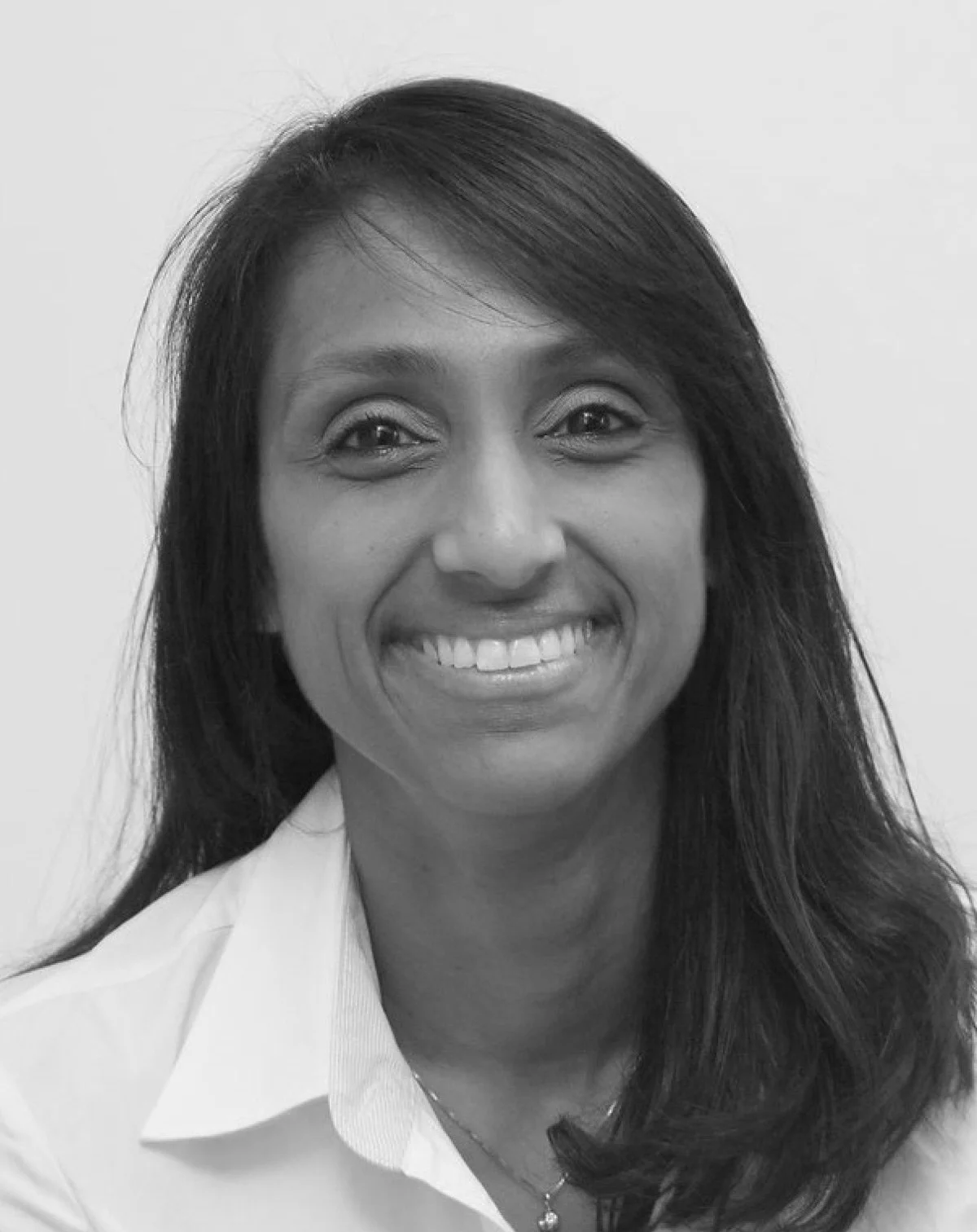 Black and white photo of a smiling woman with long dark hair wearing a white collared shirt and a necklace.