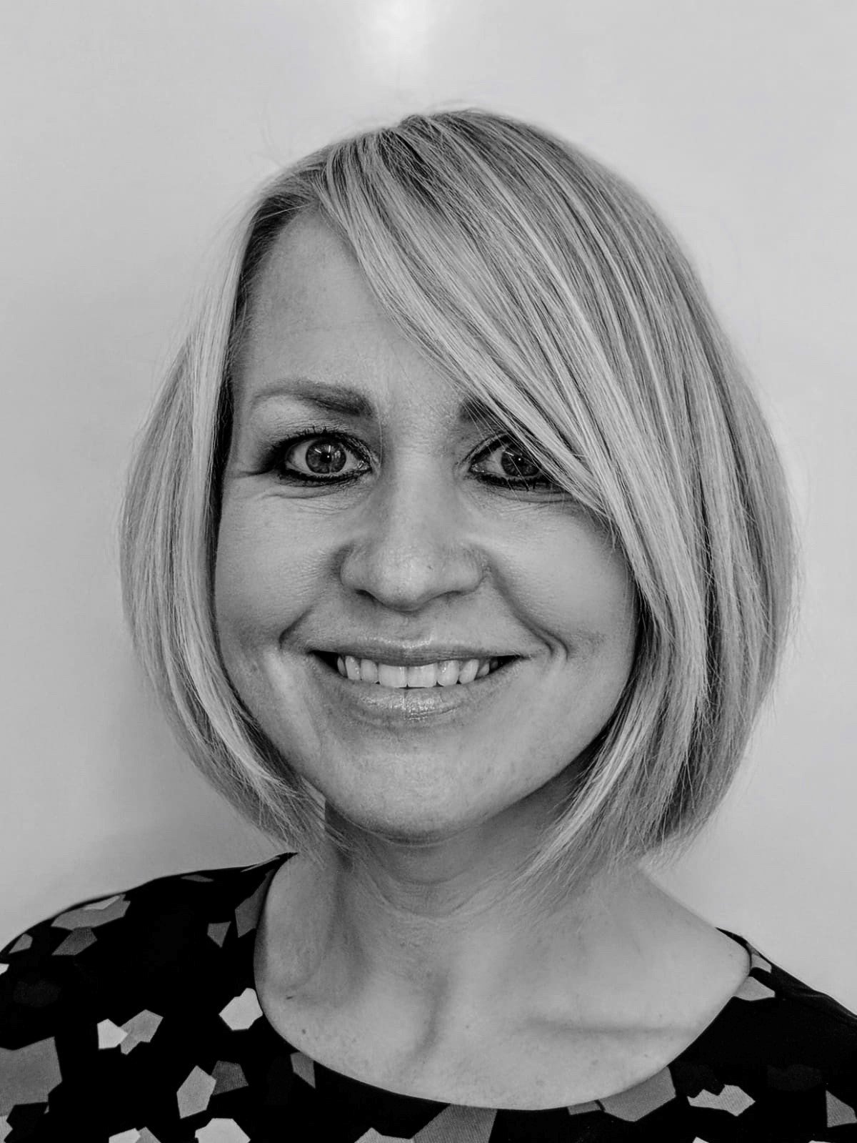 Black and white portrait of a woman with short, layered hair and a patterned top, smiling at the camera.