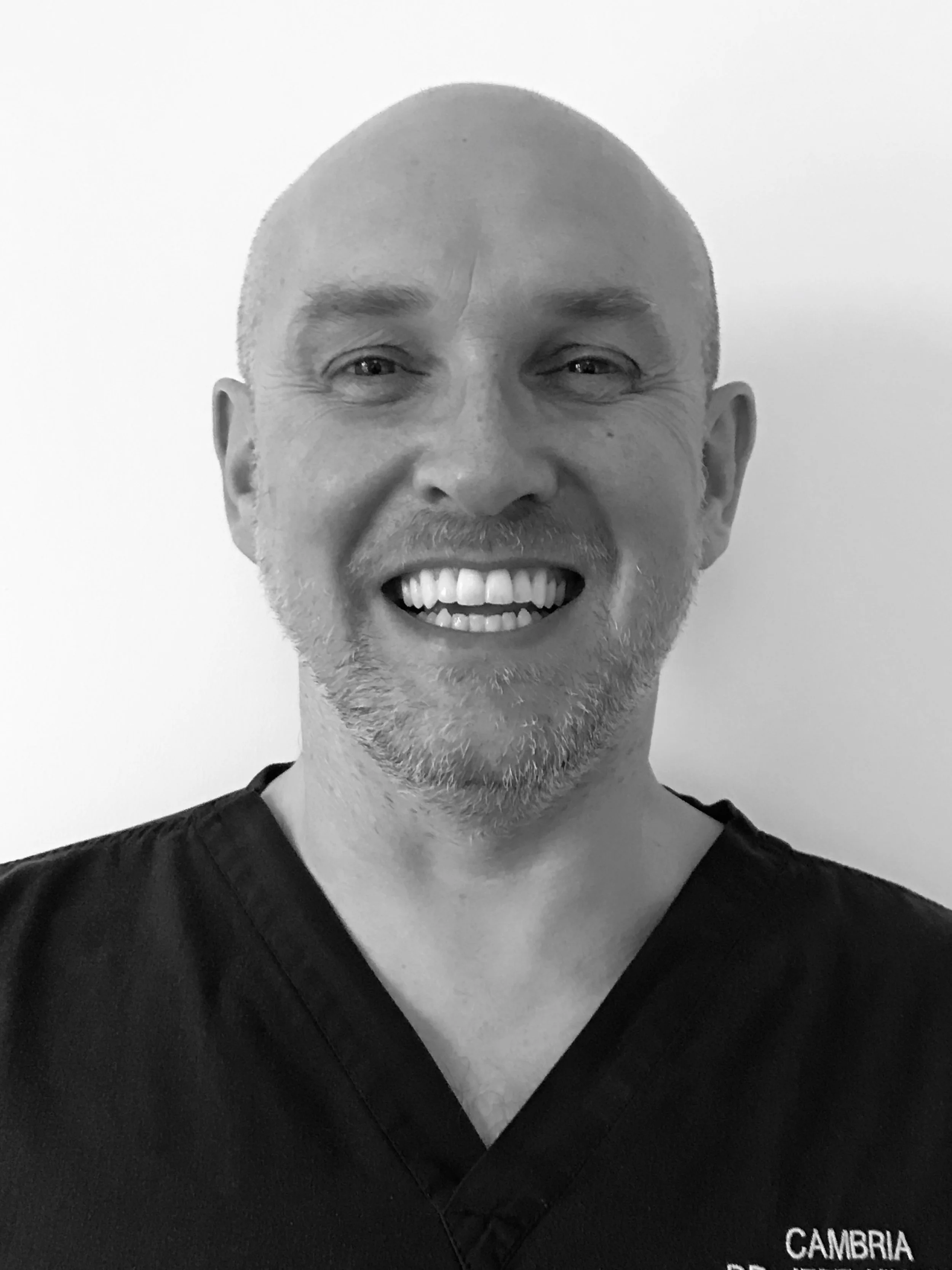 Black and white photo of Jeff Hinton with a shaved head, goatee, and wearing medical scrubs.