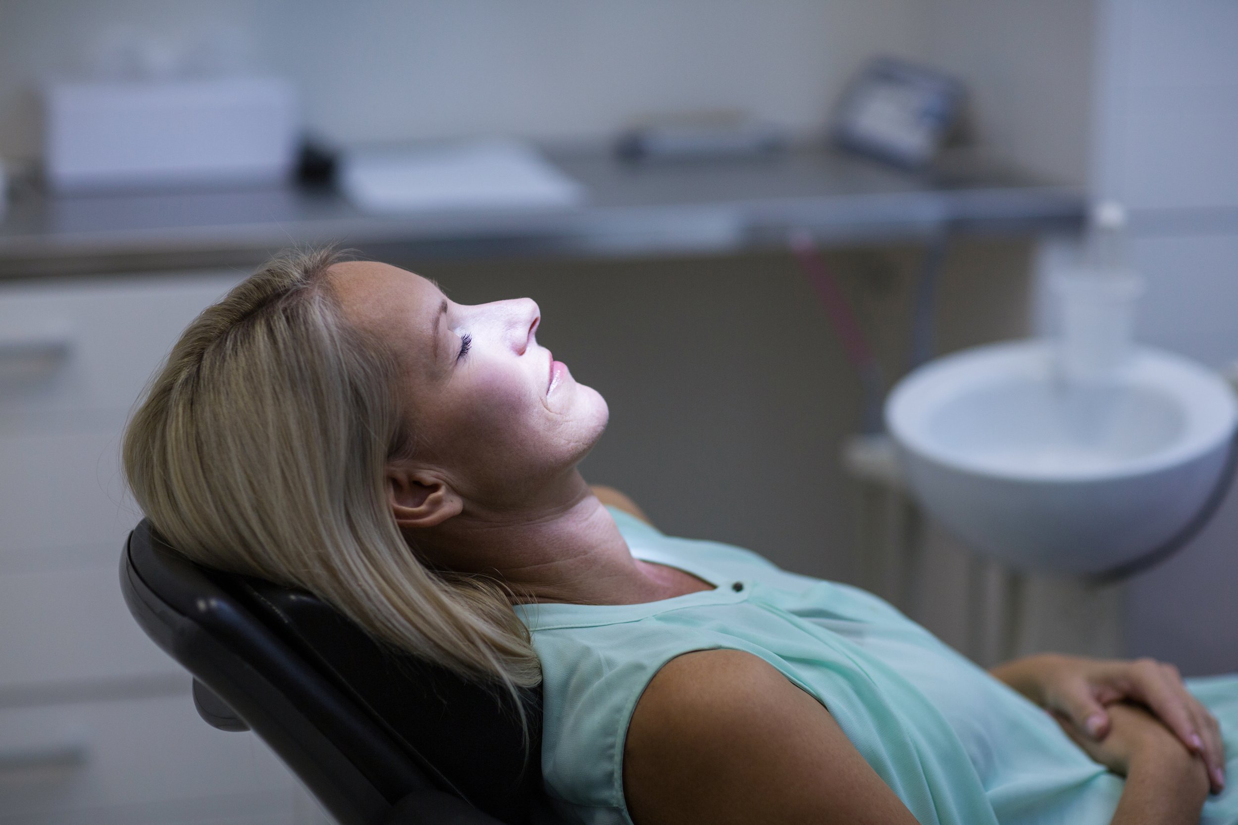 A woman lying back in a medical chair with her eyes closed, in a healthcare setting.