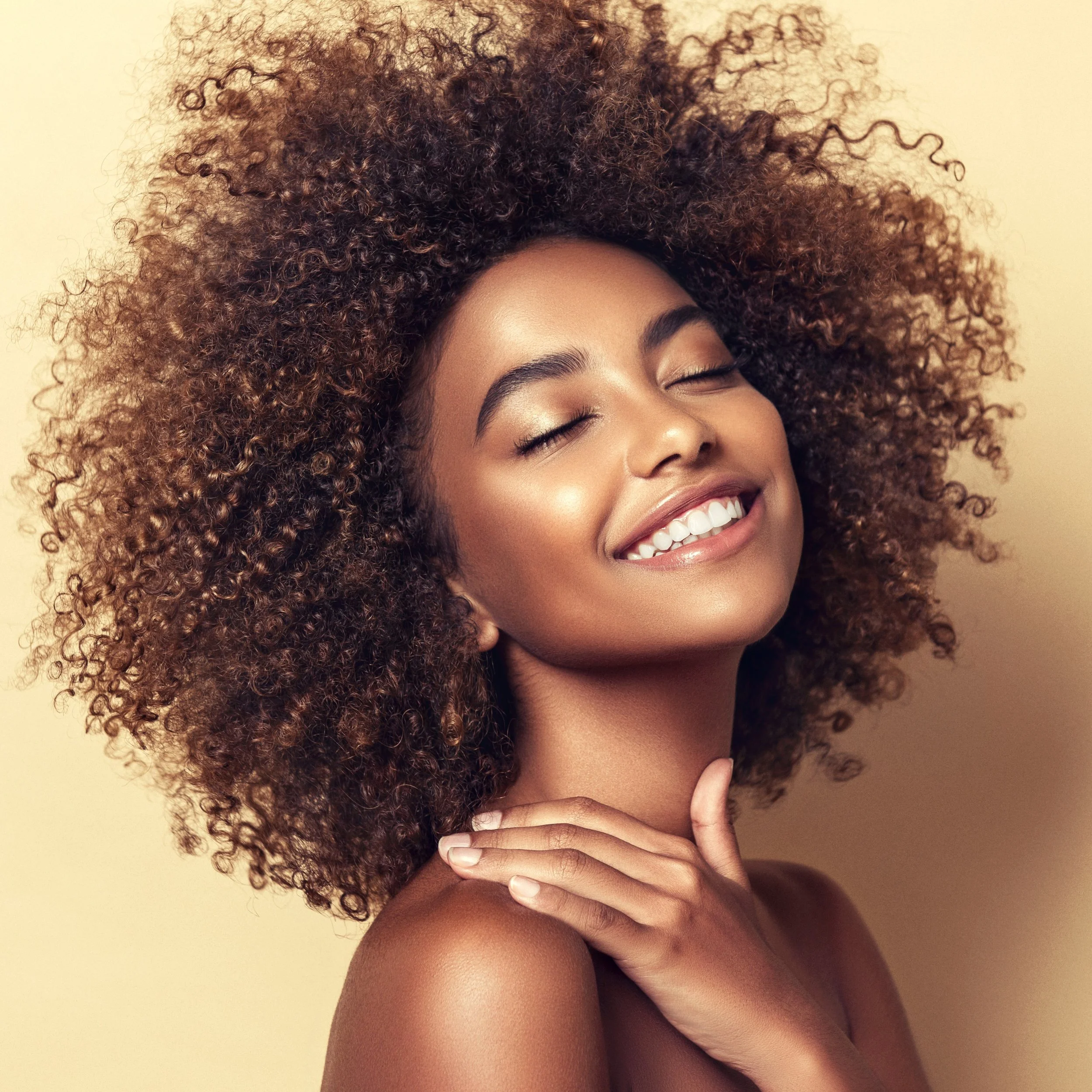 A smiling woman with curly hair and closed eyes.