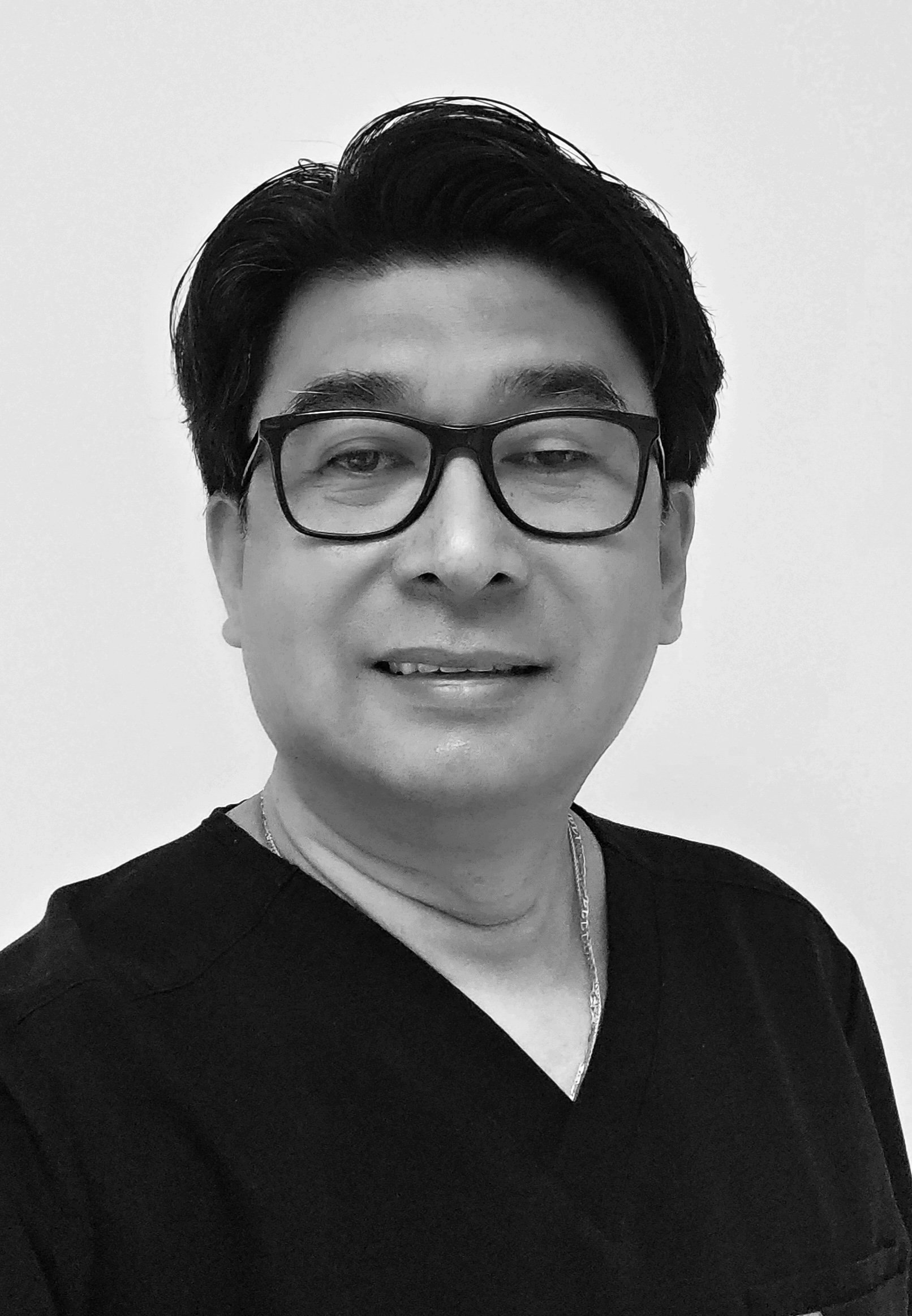 Black and white photo of an Asian man smiling, wearing medical scrubs.