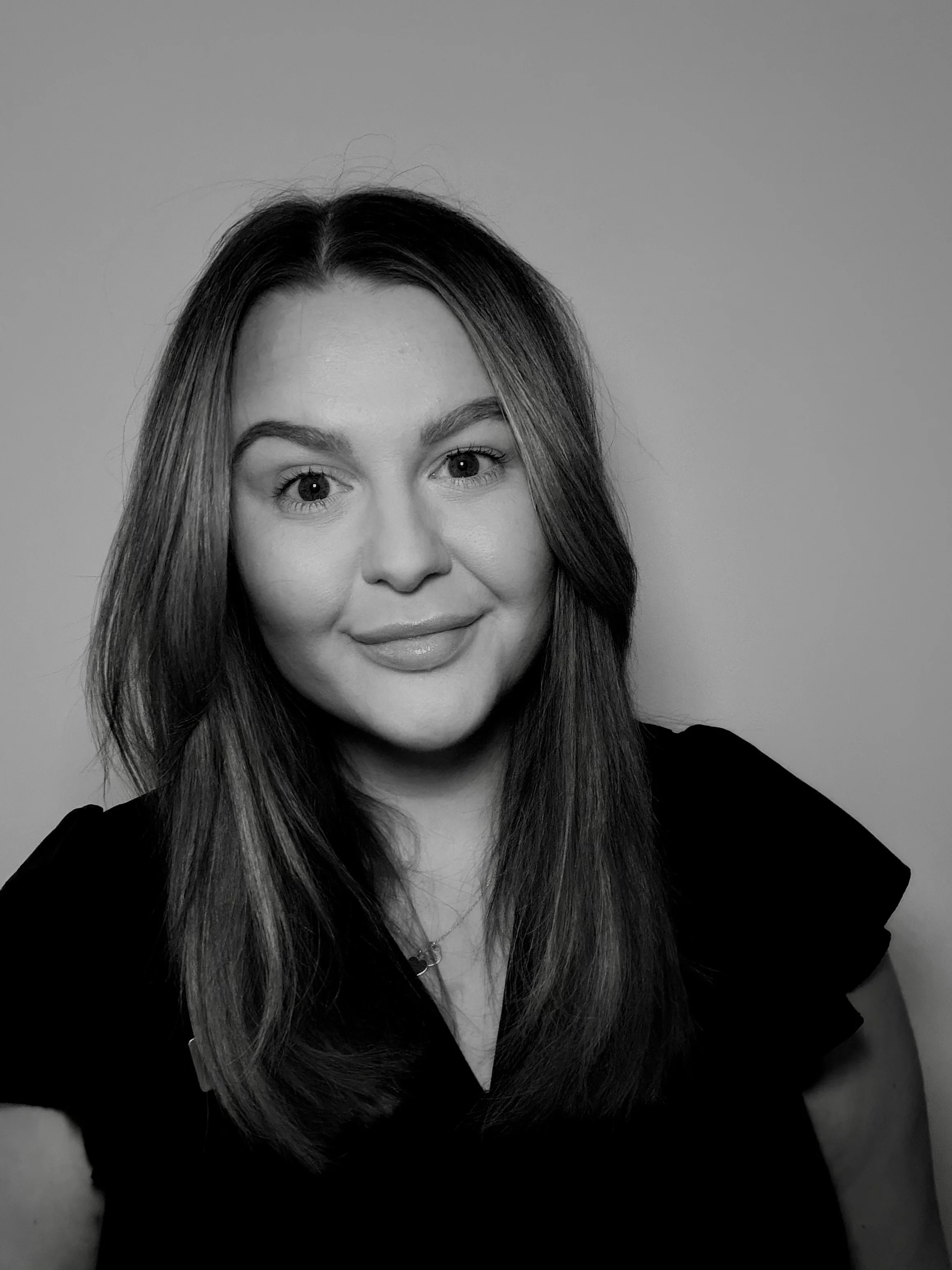 Black and white portrait of a young woman with long hair, smiling, wearing a dark top, against a plain background.