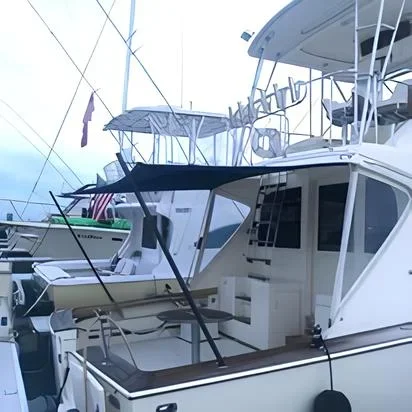 A marina with boats docked, featuring a large white yacht with a large custom Robie Canvas sun fly cover, with other boats visible in the background.