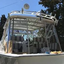 The image shows a boat with a clear canopy, and tweed sunbrella enclosure fabricated by Robie Canvas, with trees in the background. 