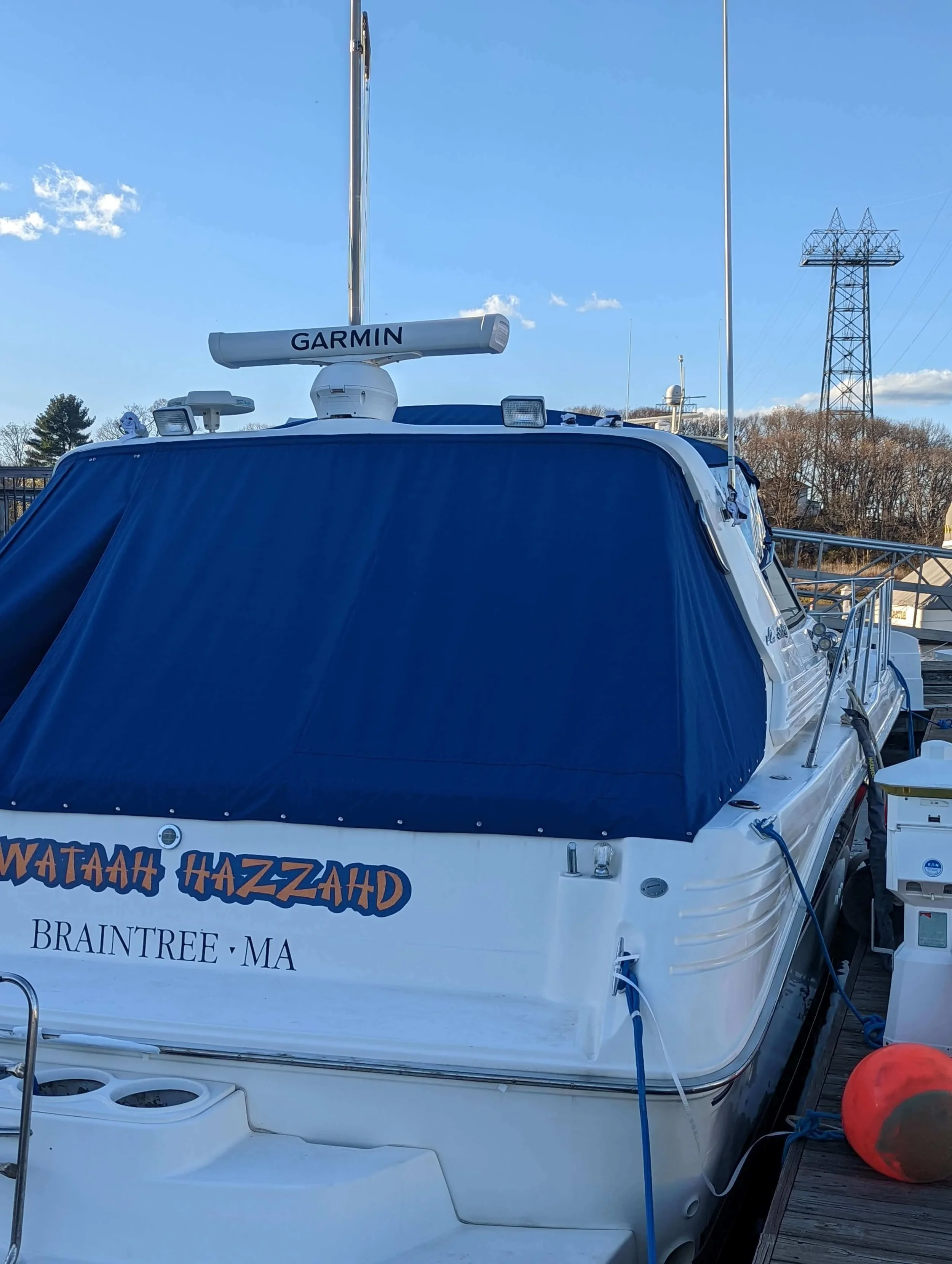 Photo of a white boat docked at a marina with a blue mooring cover custom fabricated by Robie Canvas.