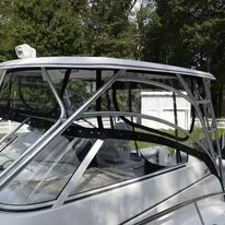 Close-up of a boat's front with a white and silver exterior, surrounded by green trees and clear sky.
