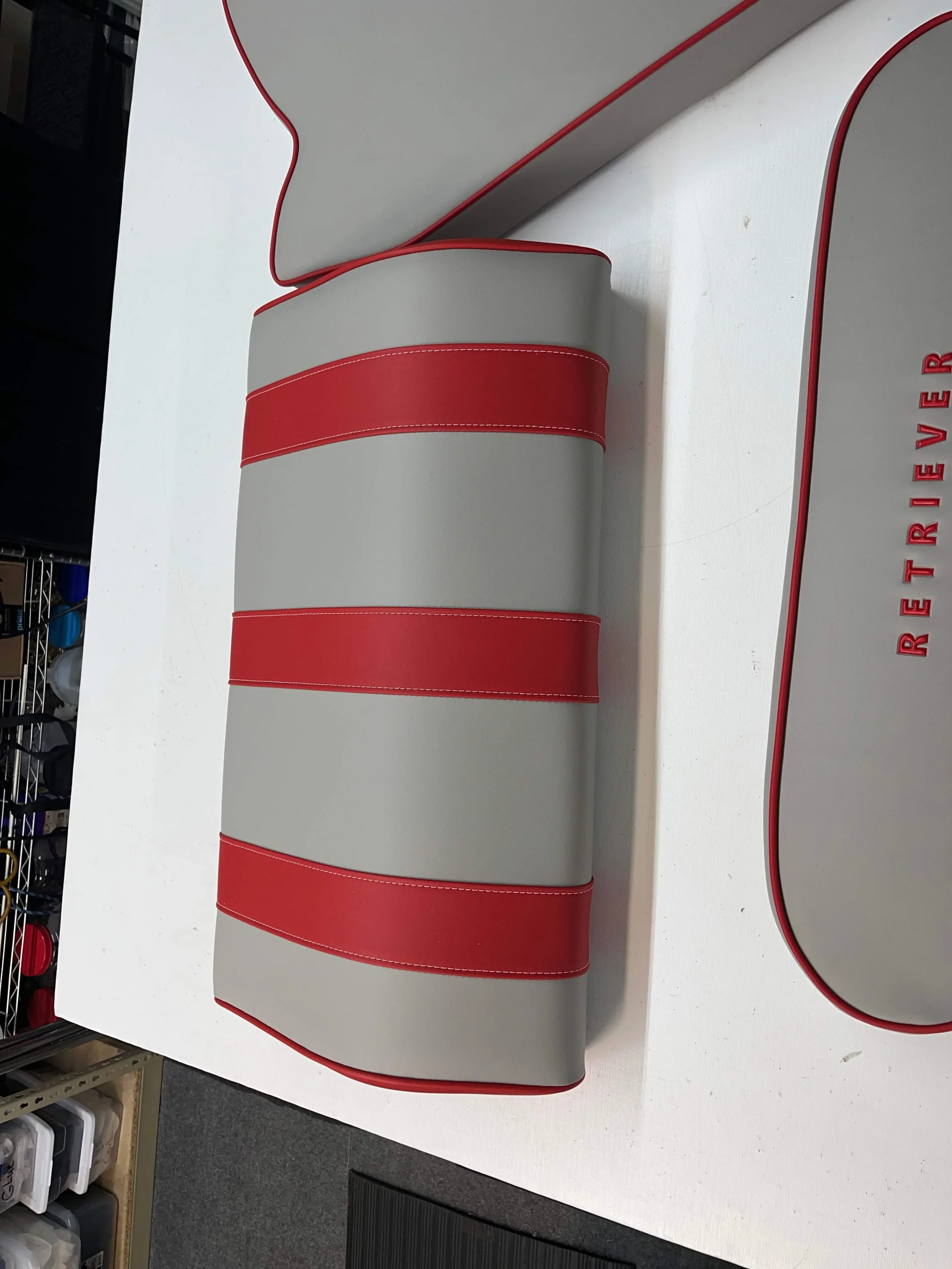 A gray headrest with red stripes resting on a white surface. The word 'RETRIEVER' is visible in red on a gray surface nearby.