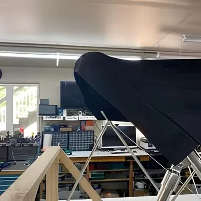 A Robie Canvas custom bimini top patterned to it's matching custom stainless frame with tools, shelves, and electronic equipment in the background.