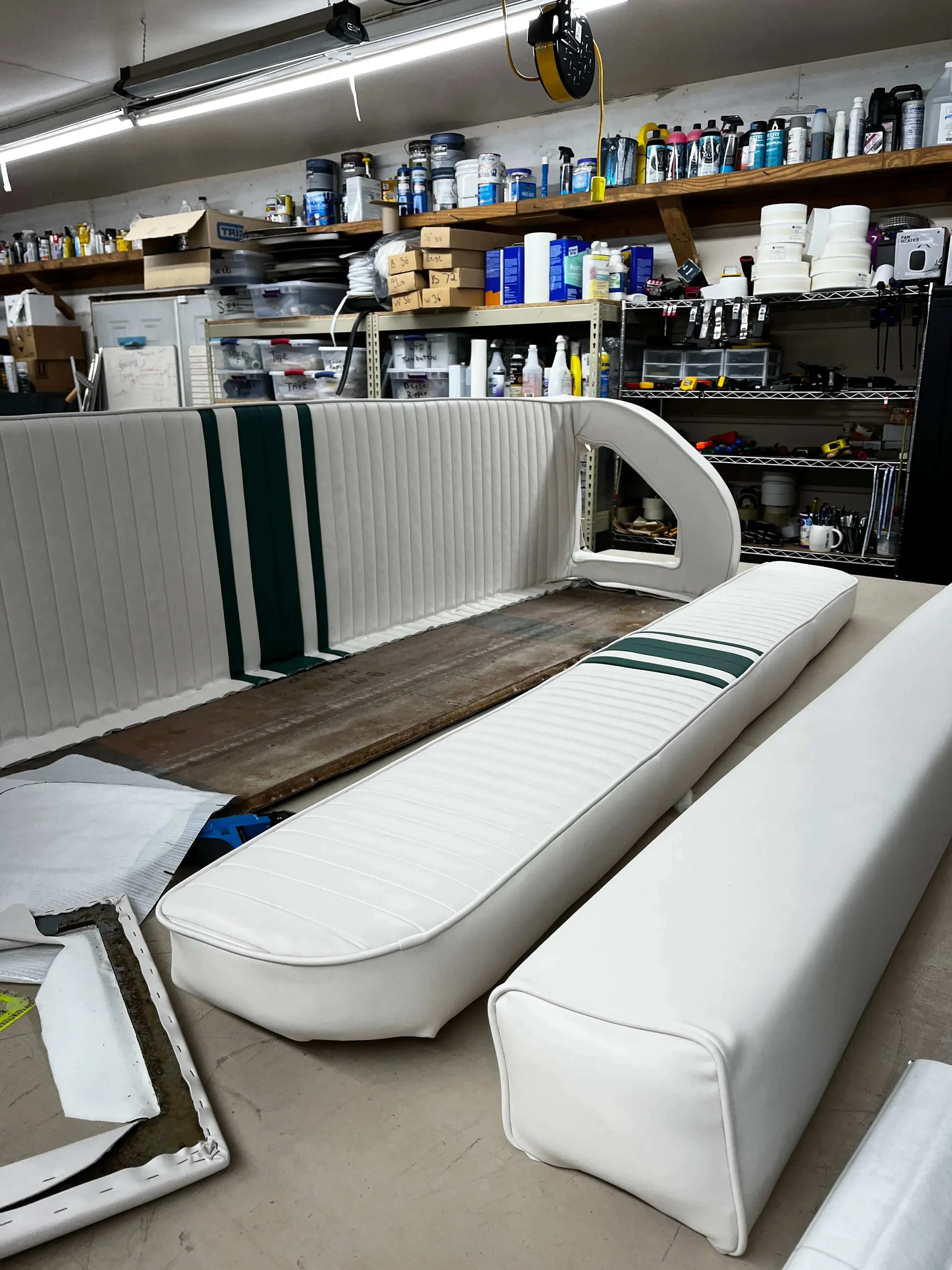 Furniture upholstery being assembled or repaired in a workshop with tools and supplies on shelves in the background.