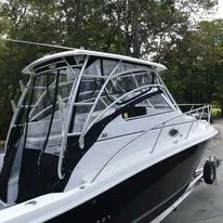 A white and black motorboat with a canopy and railings, on a trailer in a wooded area.