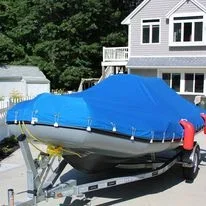 A small boat covered with a Robie Canvas custom blue mooring cover, on a trailer in a driveway.