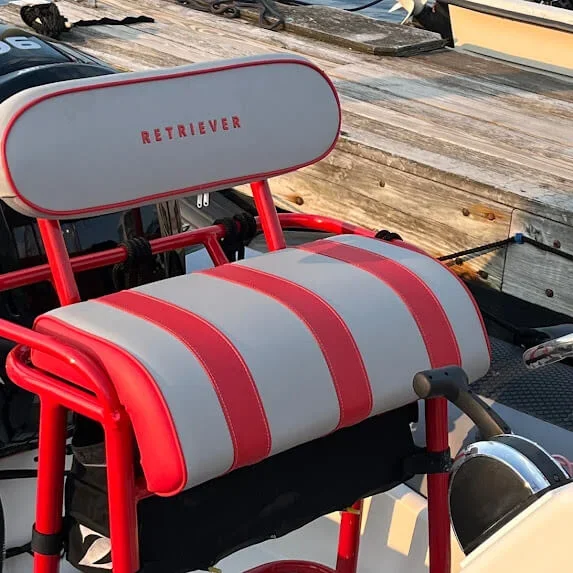 Robie Canvas custom red and gray center console seat with the word 'Retriever' on the backrest, positioned on a dock near boats.