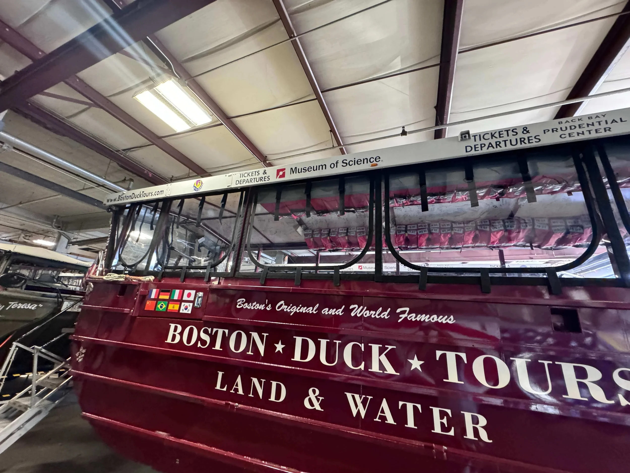 Duck boat tour vehicle with Robie Canvas enclosure panels, parked indoors at a museum or tour center, advertising Boston duck tours on the side.