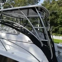 Close-up of a large boat with a black safety railing and multiple windows, docked near trees and greenery.