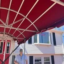 A person standing under a red canopy outside a house with white siding and blue windows.