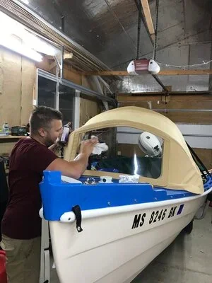 A man working on a boat inside a garage, with tools and a blue object nearby.