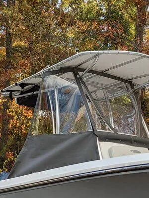 Close-up of a boat's canopy with clear plastic side panels, set against autumn-colored trees.