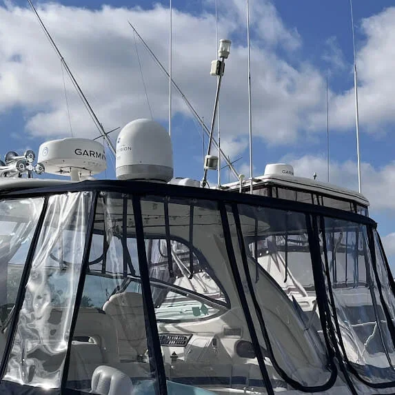 Close-up of a boat's helm with a clear protective cover, with multiple antennas and navigation equipment on the top, under a partly cloudy sky.